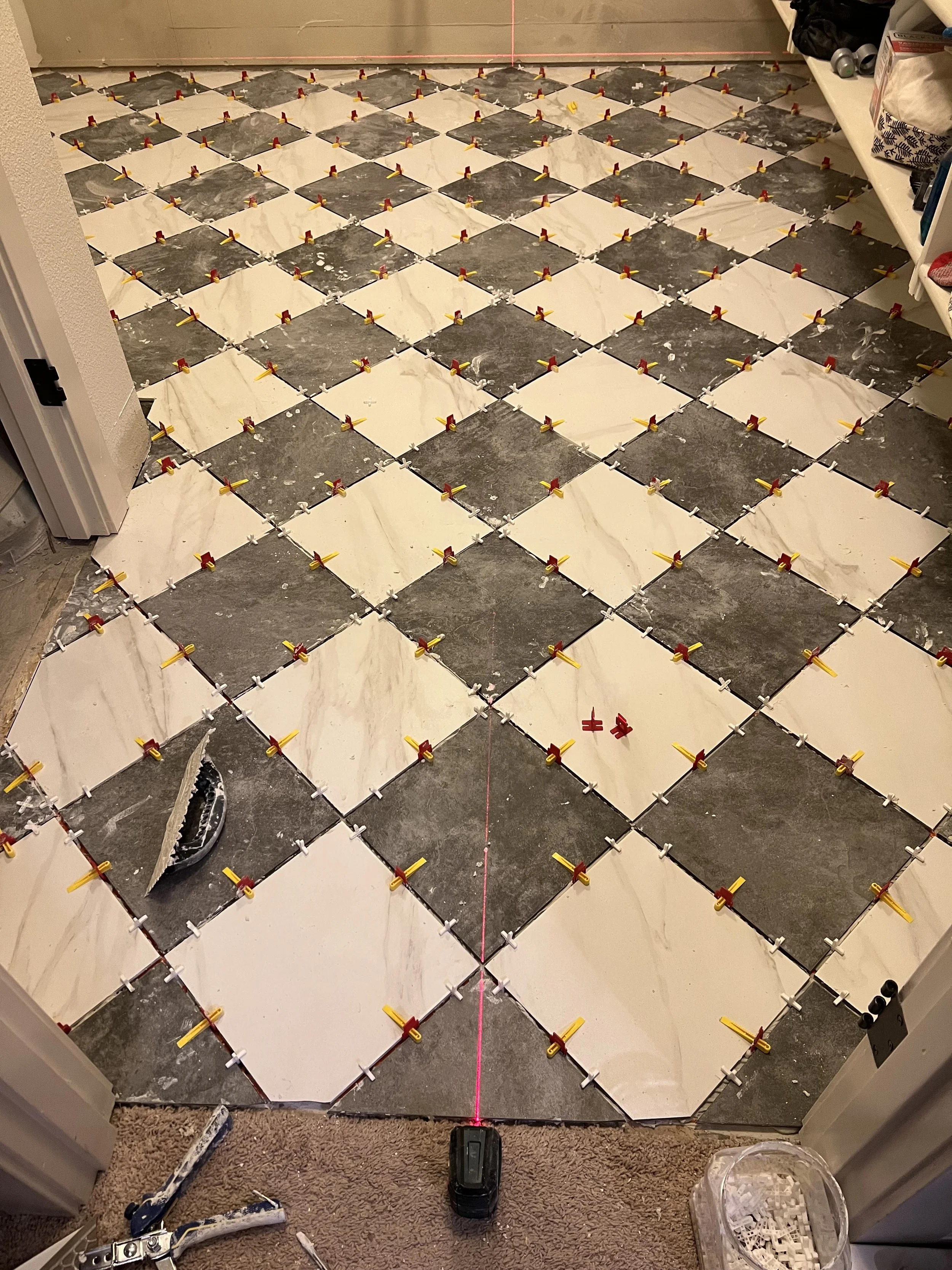 Mid renovation: A close view of the checkerboard marble tile floor partway through installation with leveling spacers