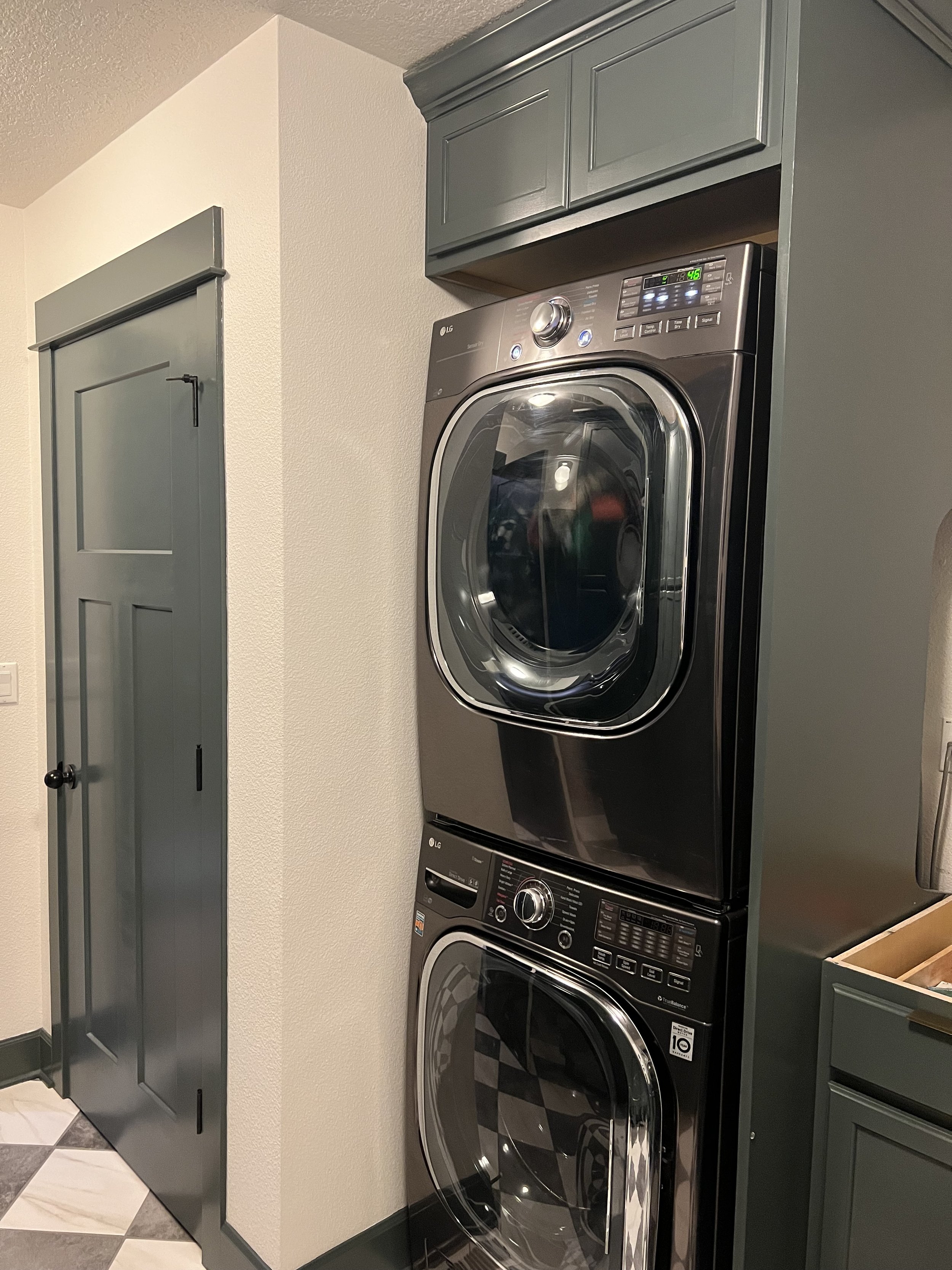 Mid renovation: A stacked washer and dryer set into pewter green cabinetry beside a dark painted door.
