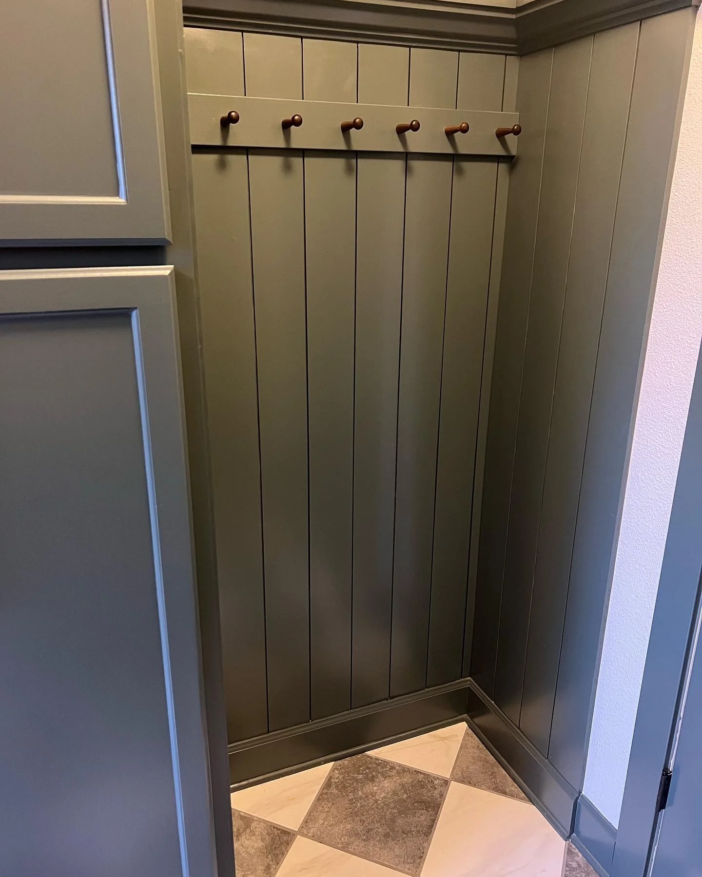 Mid renovation: Pewter green vertical plank paneling with a row of black walnut wall hooks above a bench nook