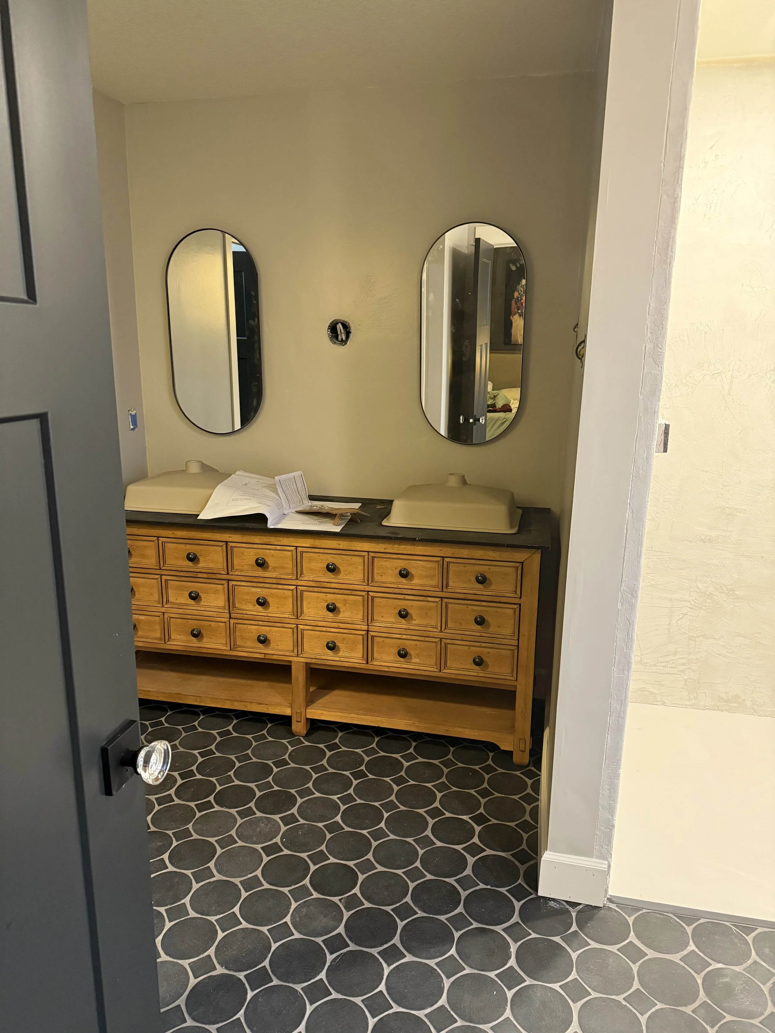 bathroom vanity during installation with two mirror medicine cabinets on the wall and black slate tile floor.