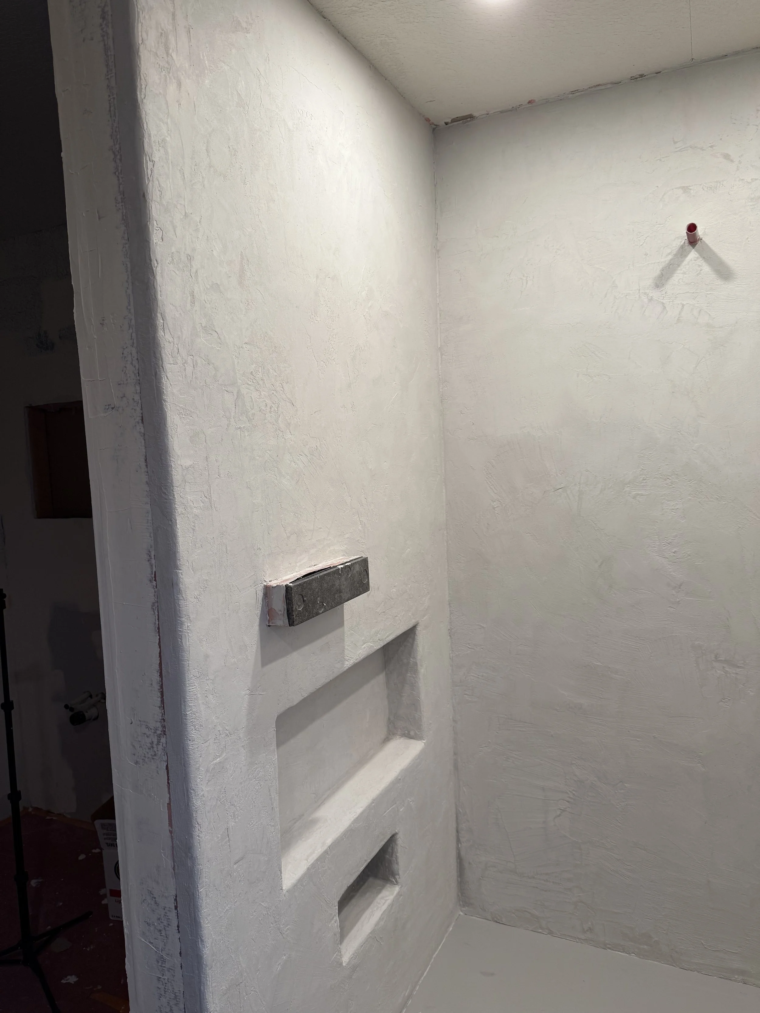 Textured microcement being applied to a bathroom wall with a built-in niche.