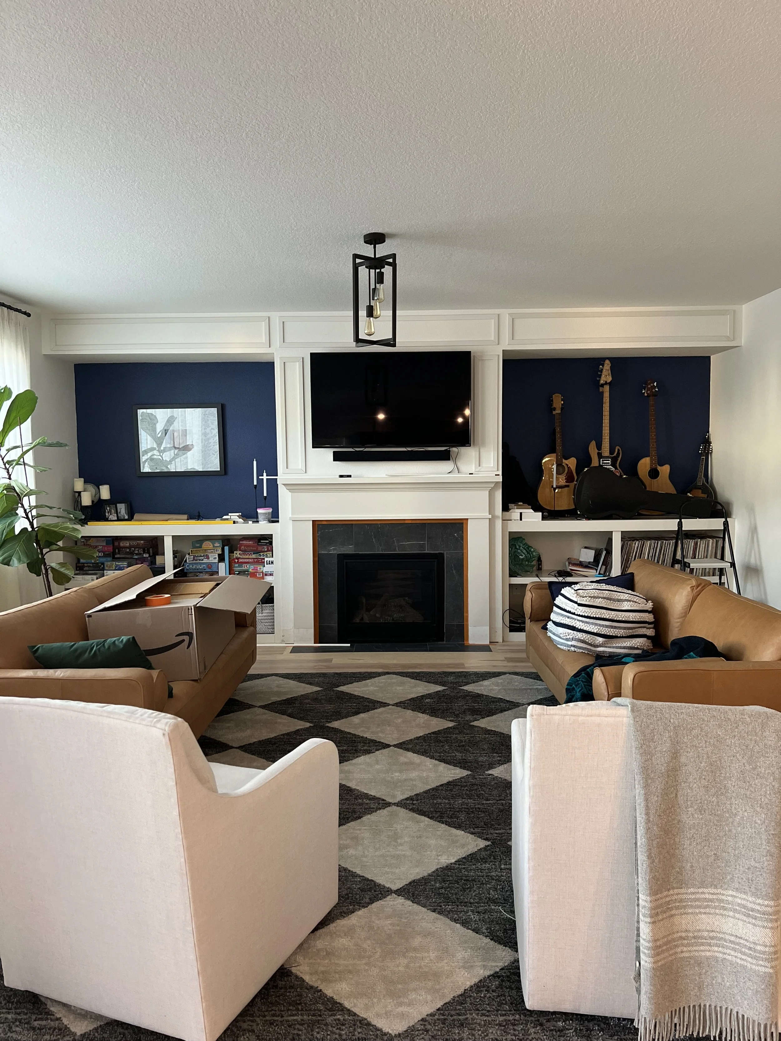 A living room mid-renovation with the built-ins primed white, a checkerboard rug going down, and furniture pushed aside.