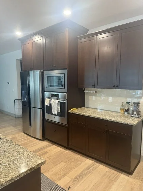 Before renovation: a kitchen with dark brown cabinets, stainless appliances, and a tile backsplash