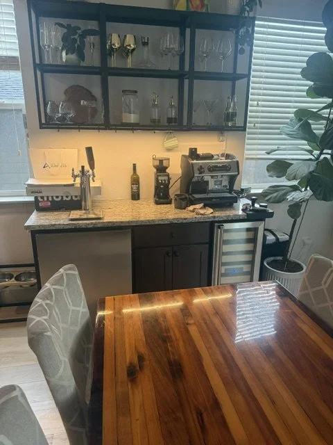 Before renovation: a wide view of a kitchen with dark brown cabinets, a granite island, and a stainless hood.