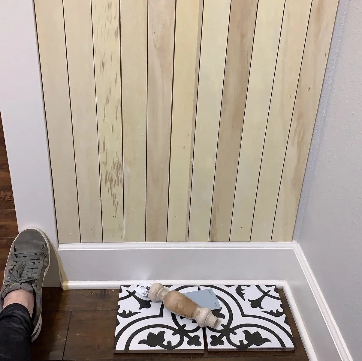 Wood plank paneling being installed on a powder room wall, with a patterned tile sample on the floor.