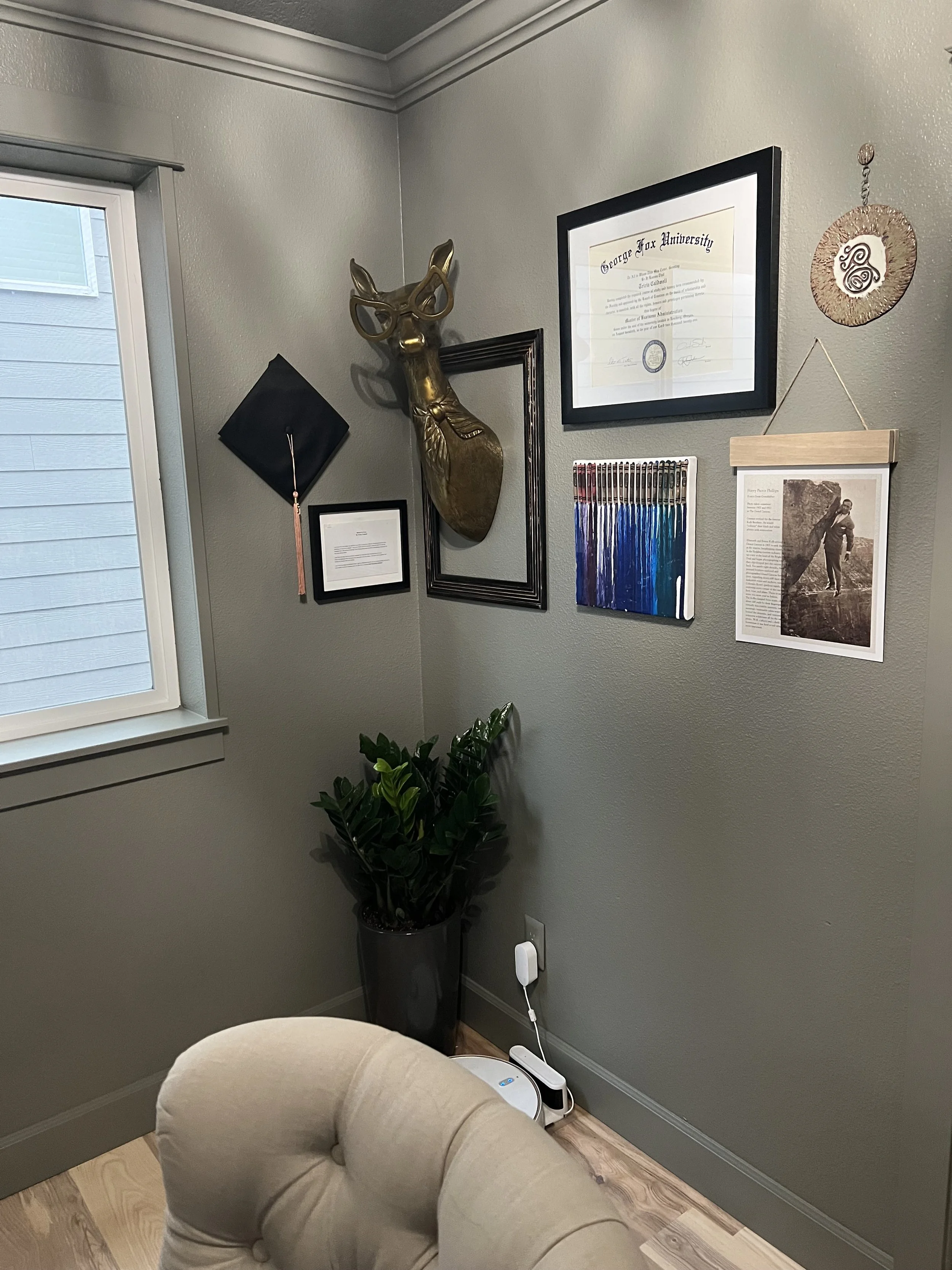After renovation: A home office corner with framed art, a mounted deer head, and a cushioned chair against gray-green walls.