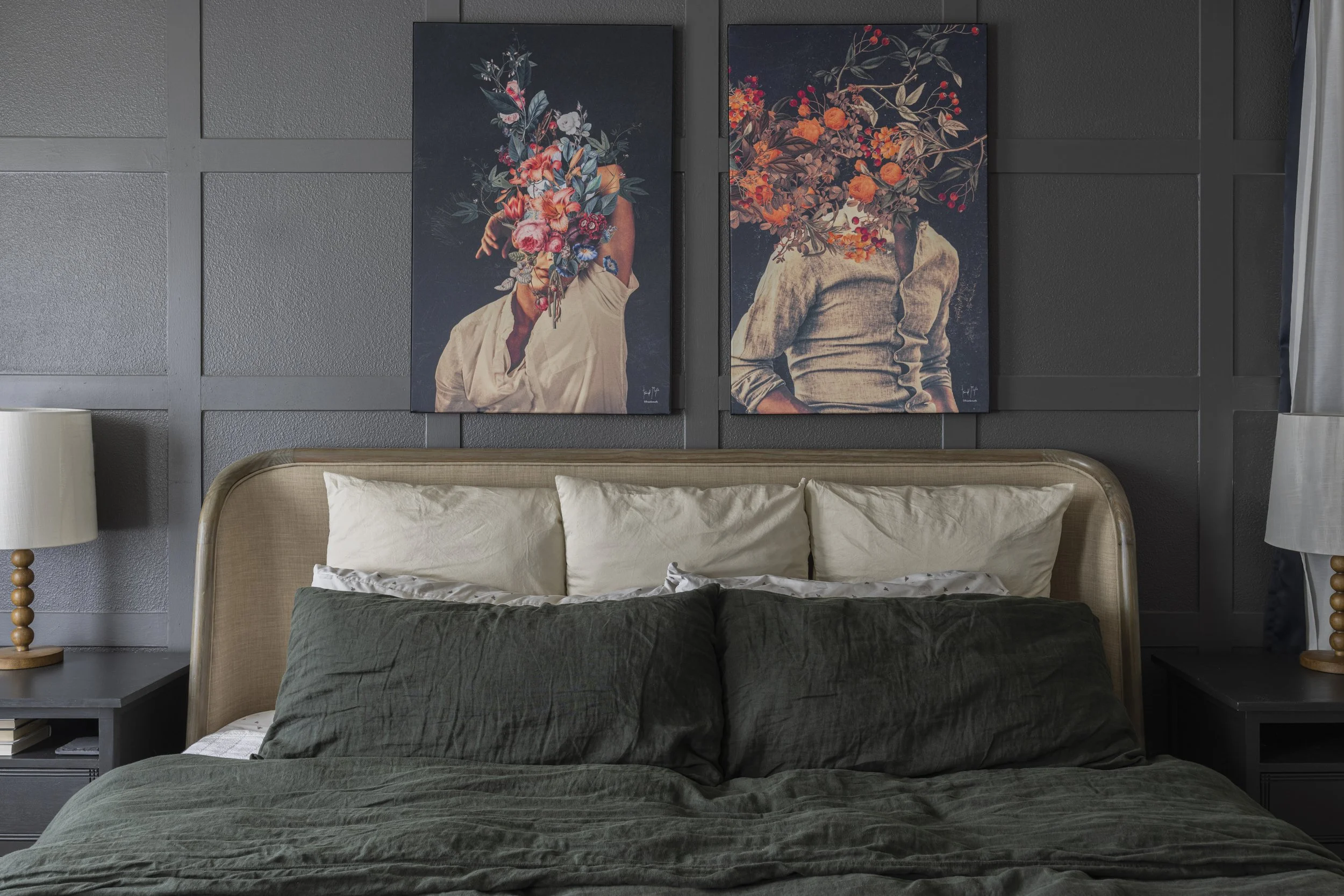 A bedroom corner with dark green bedding, framed prints, and an upholstered headboard against a dark wall.