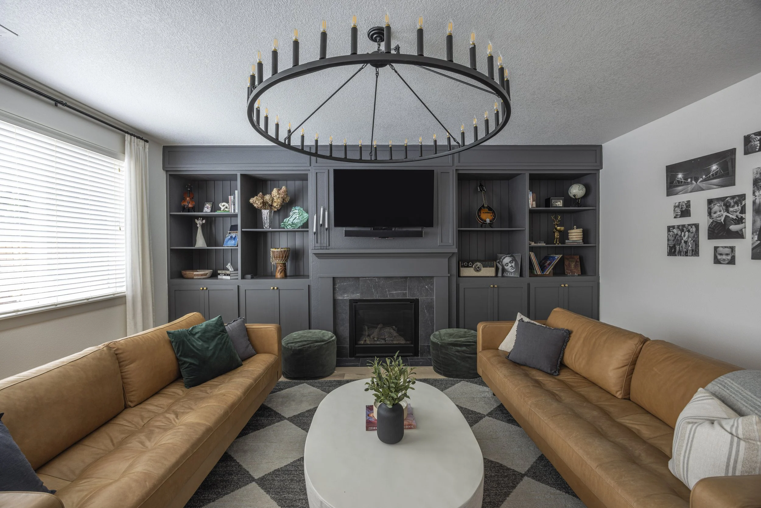 A finished living room with built-in shelving, a tan leather sofa, a round table, and a black ring chandelier.