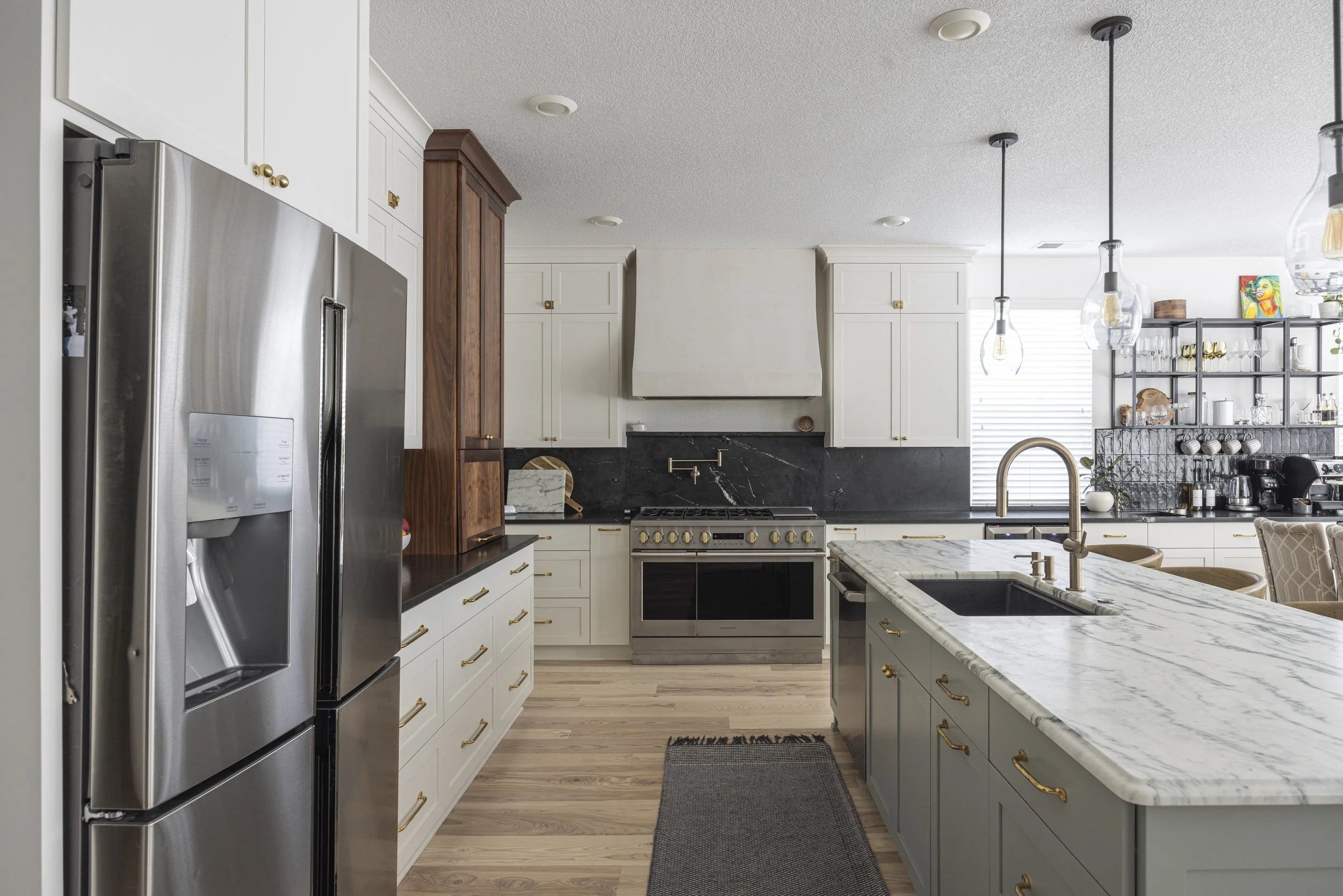 A kitchen with white cabinets, stainless appliances, a marble island, and a dark tile backsplash.
