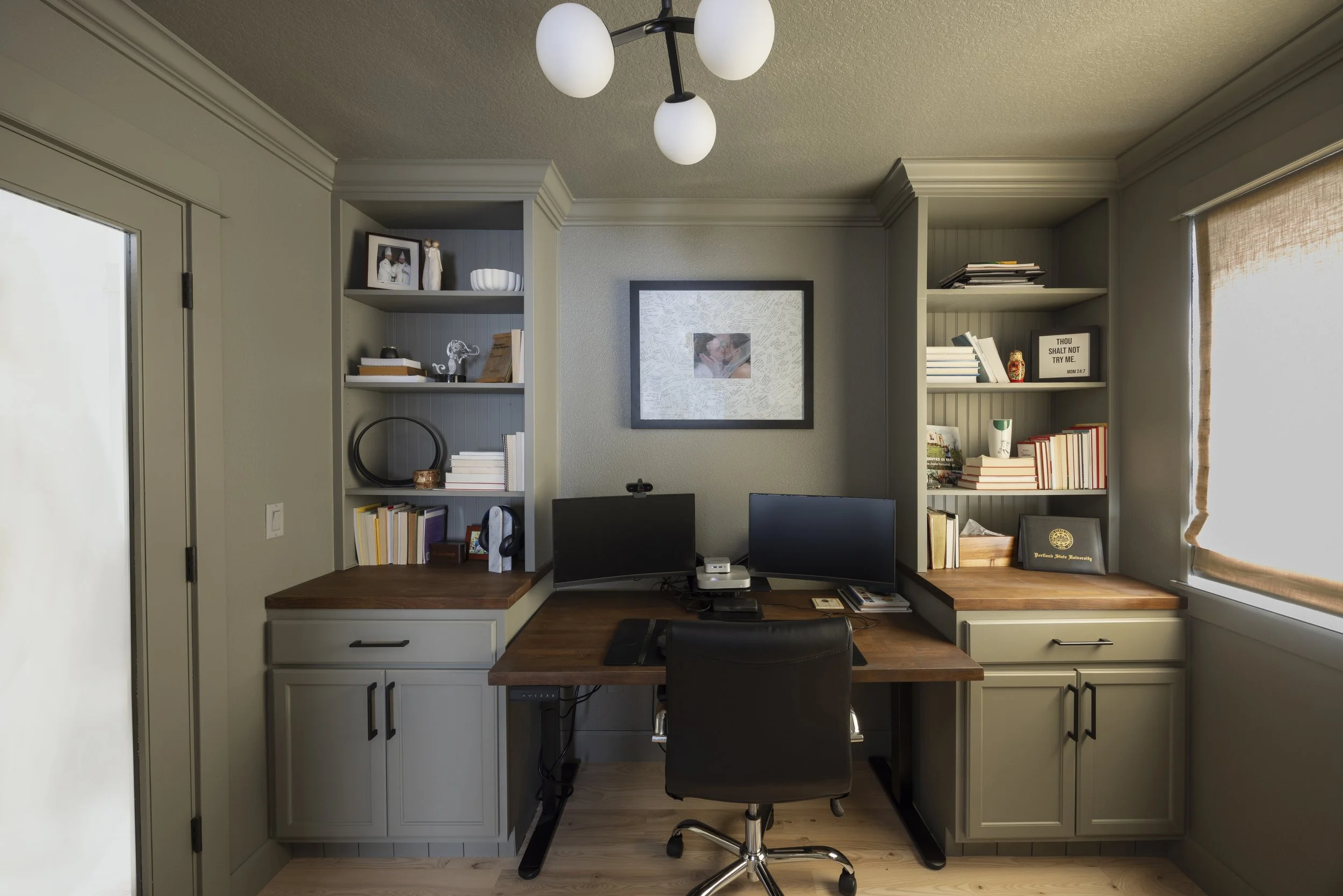 After renovation: A finished home office with a custom L-shaped wood desk, built-in shelving, and a globe pendant light.