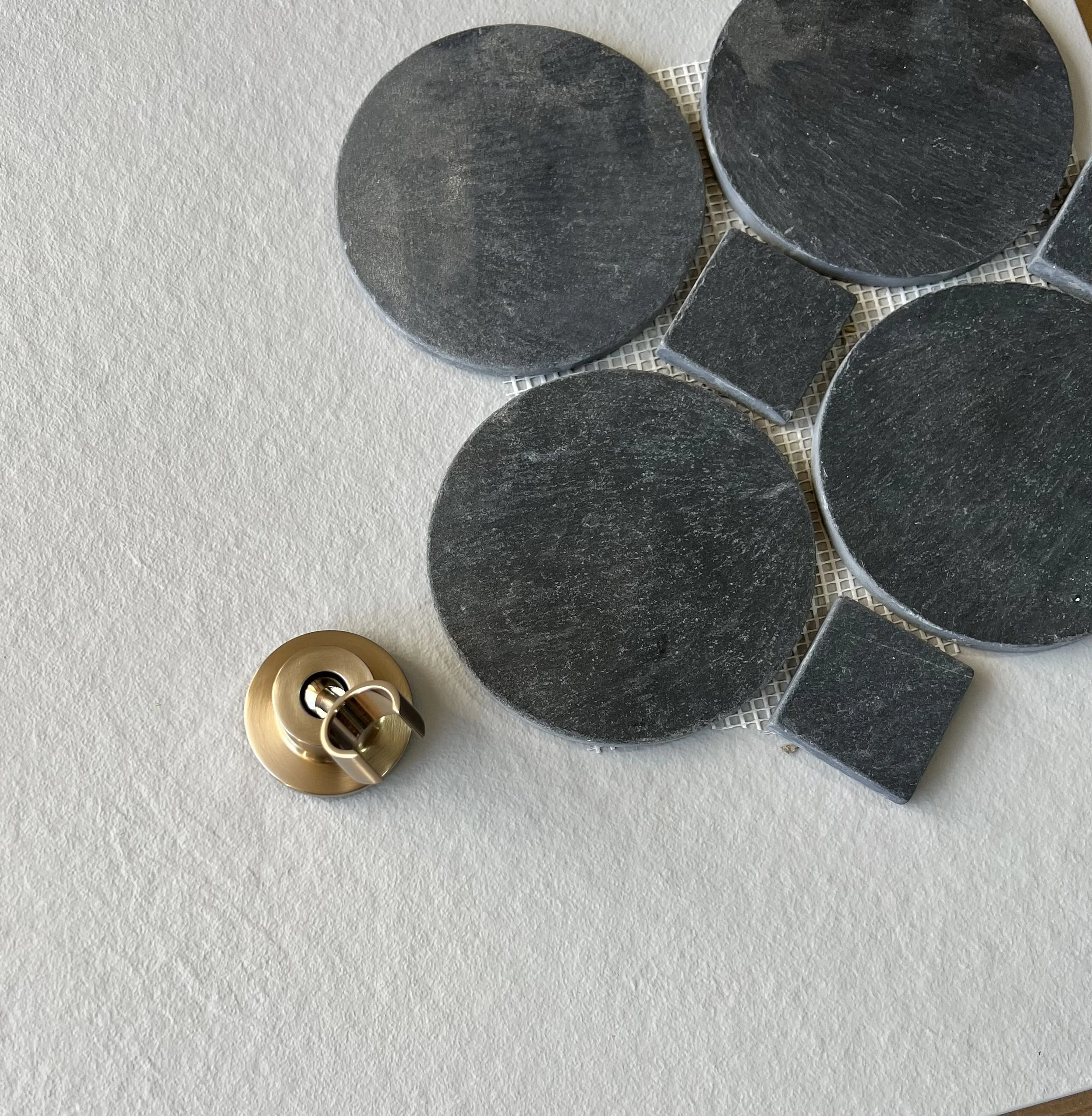 A close view of black mosaic stone tile on mesh backing beside a brass drain fixture.