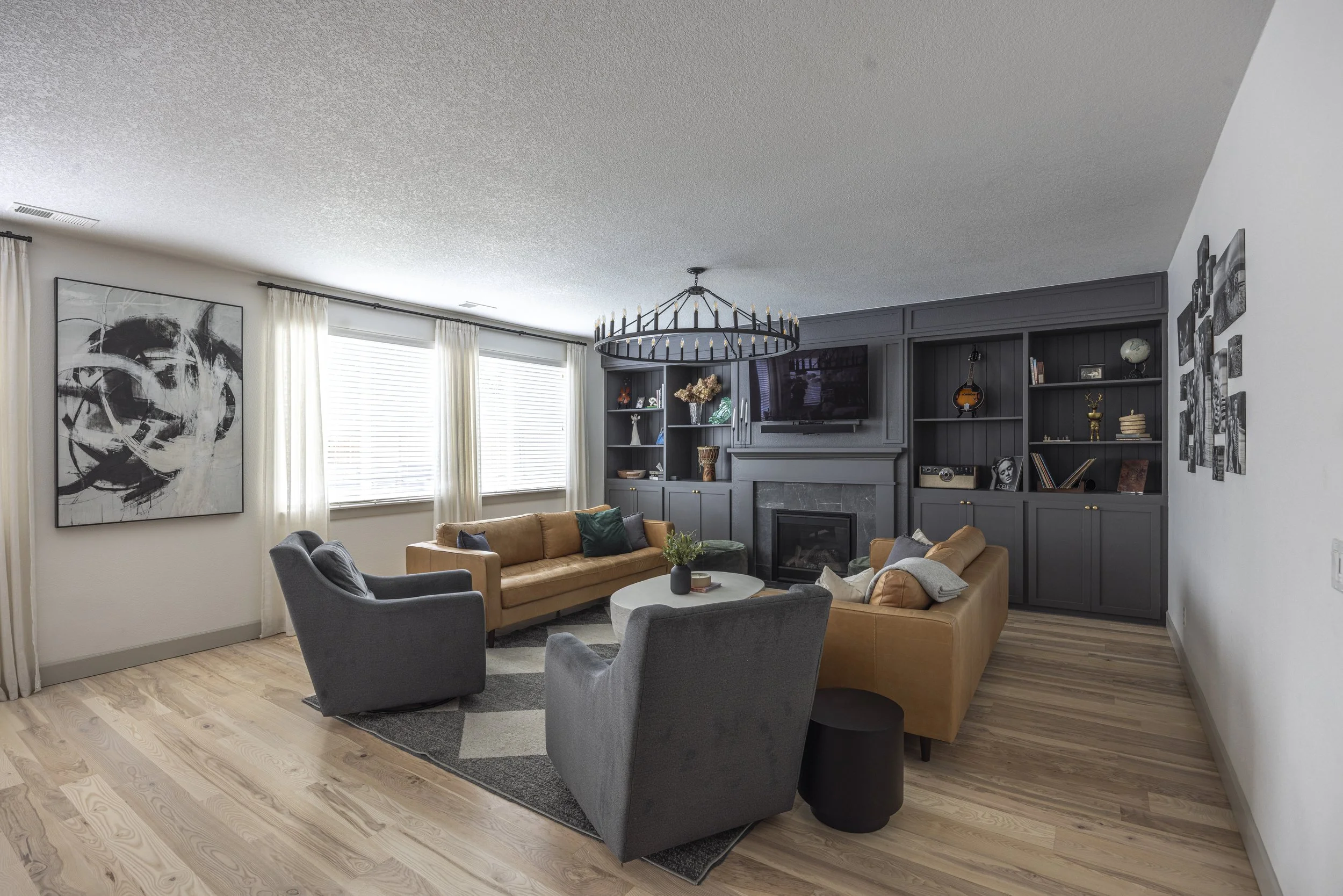 A finished living room with white walls, dark grey built-ins flanking the fireplace, a tan leather sofa, and a checkerboard rug.