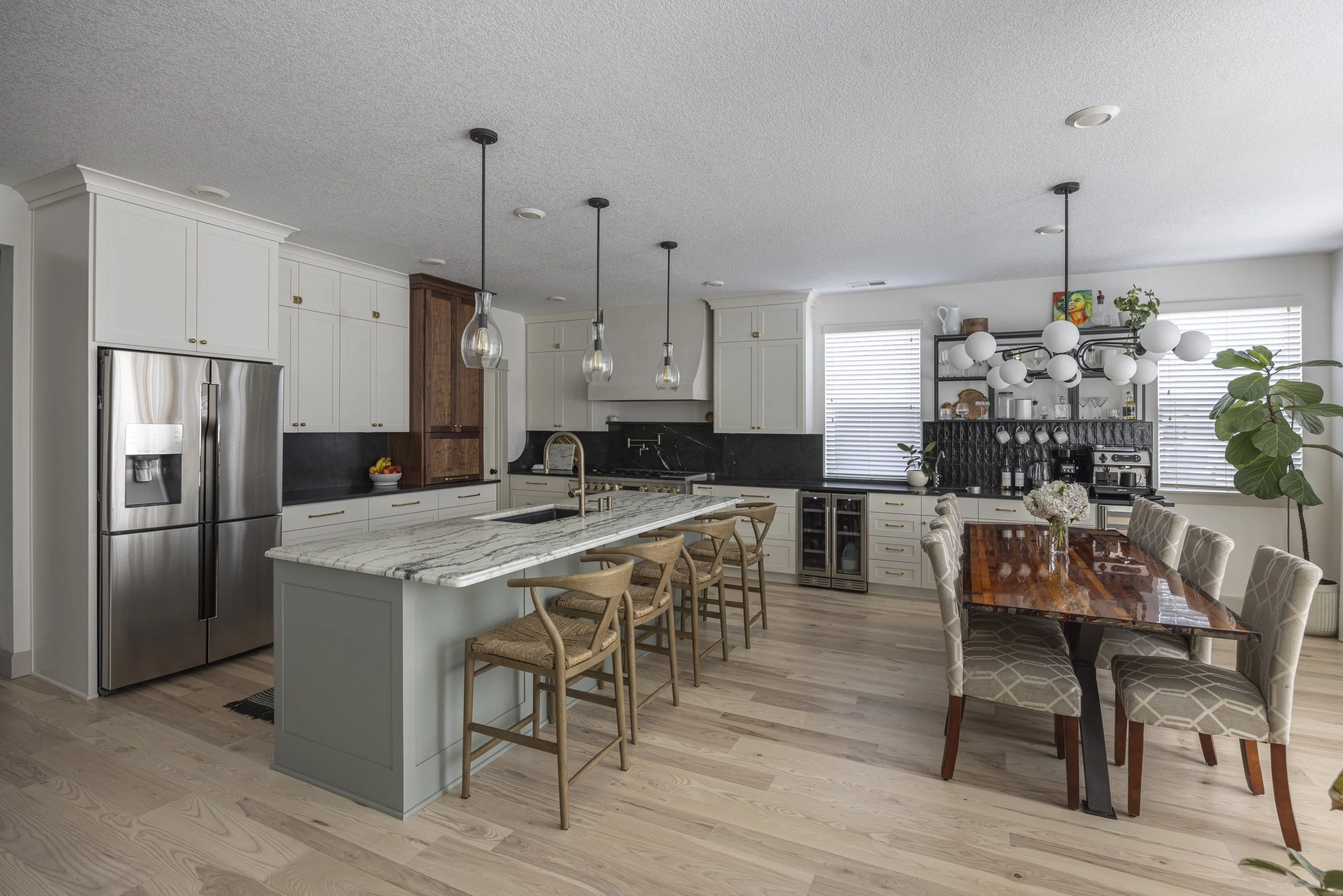 A wide view of a finished kitchen and dining space with white cabinets, a marble island, and a blue island base.
