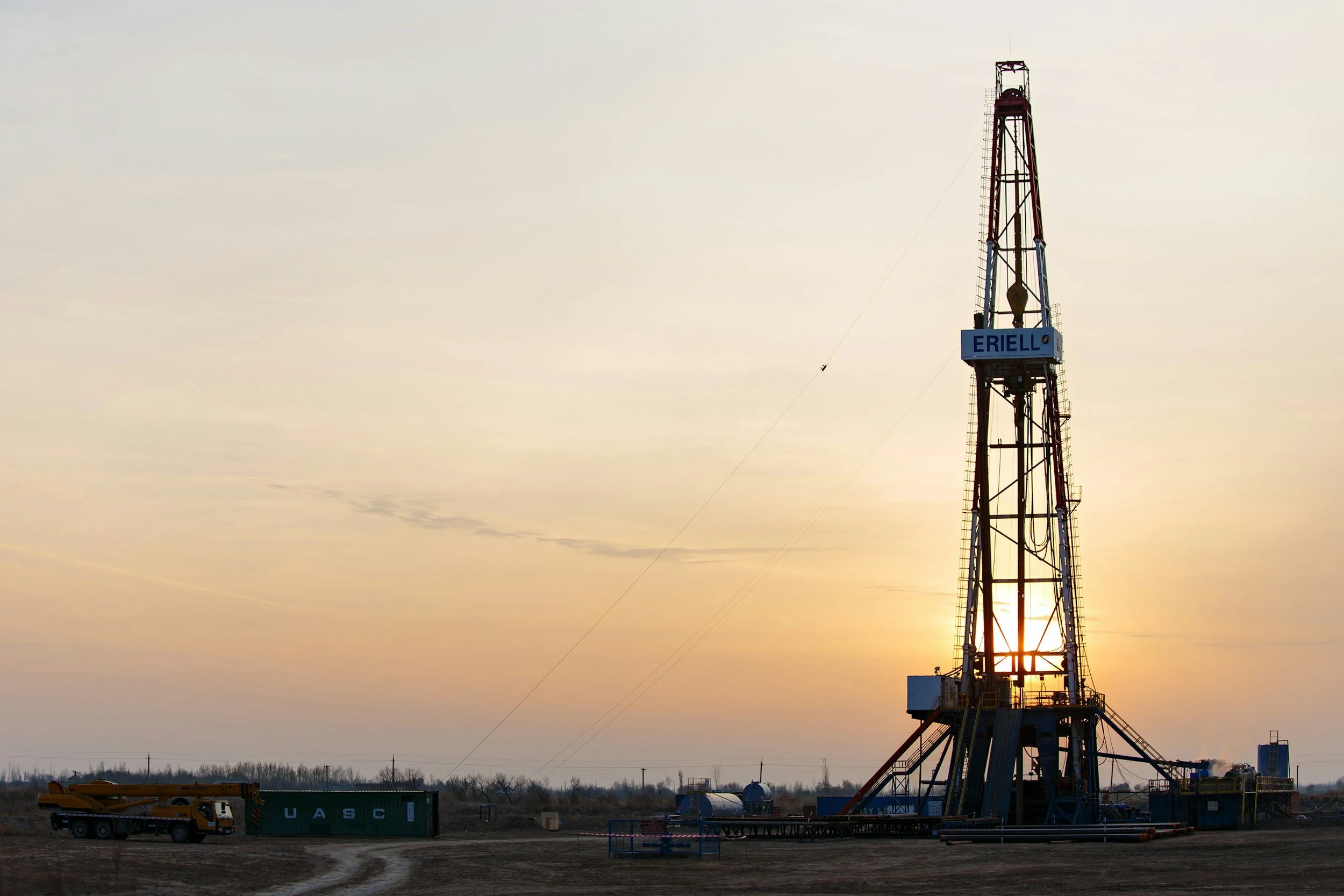 An oil drilling rig on a flat landscape with a sunset sky in the background.