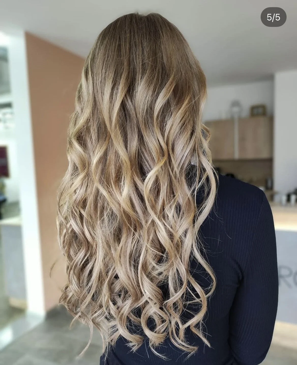 Der Rücken einer Person mit langen, blond, gewellten Haare, die in einen modernen, hellen Raum mit Küchenhintergrund schauen.