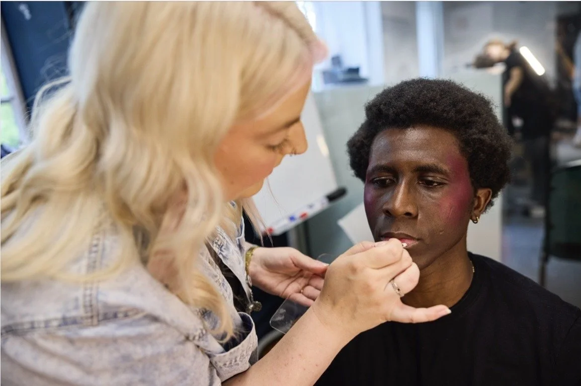 Eine Make-up-Künstlerin trägt Make-up auf das Gesicht eines Mannes auf sich, der bereit ist, für ein Fotoshooting oder eine Veranstaltung fertig gemacht zu werden.