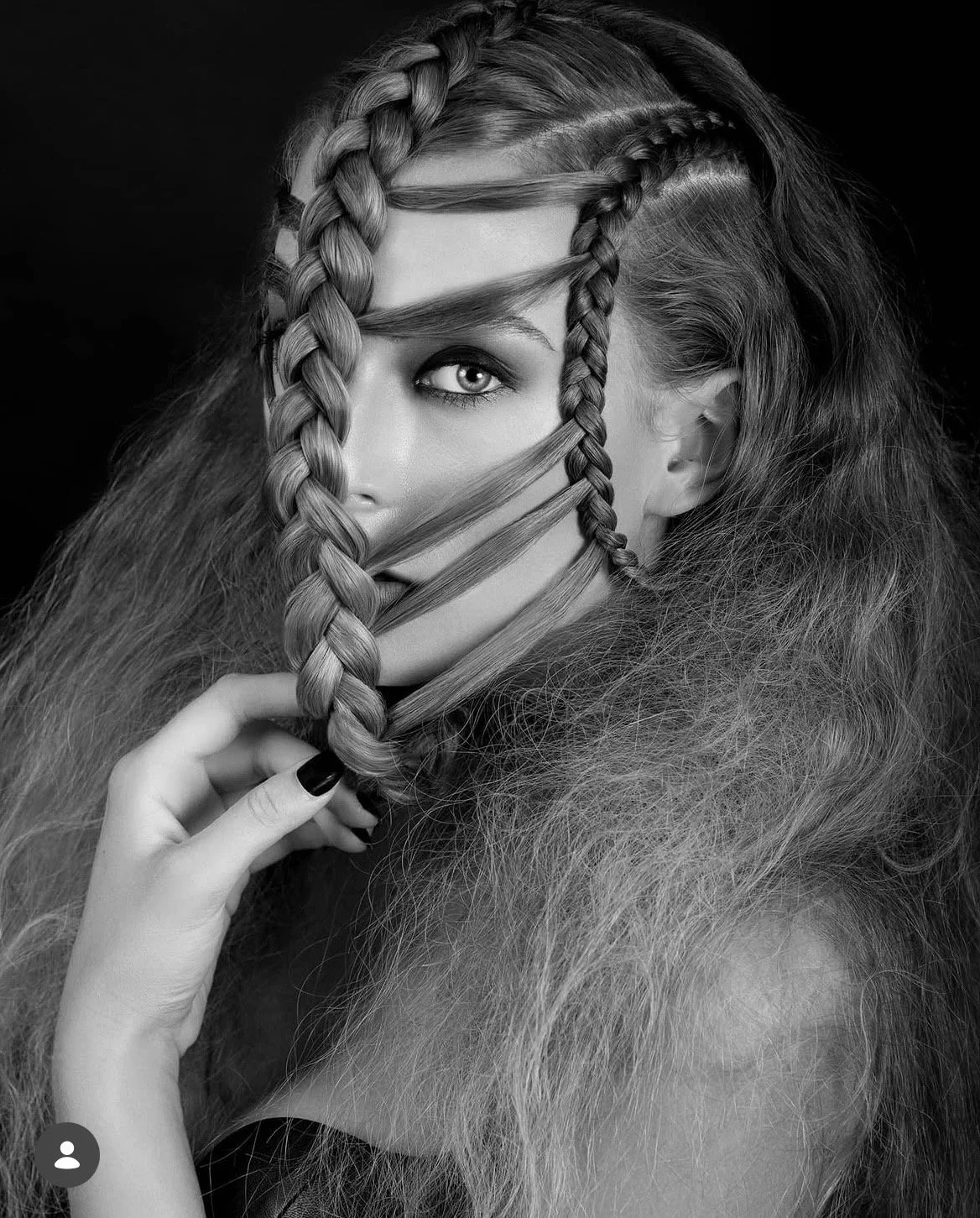 Schwarz-Weiß-Fotografie eines Mädchens mit langen, welligen Haaren und geflochtenen Strähnen, das einen Blick in die Kamera wirft.