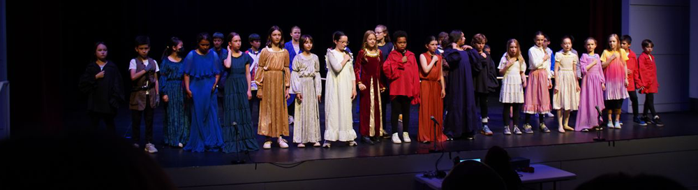 Children standing on stage, dressed in colorful costumes, participating in a performance or school play.