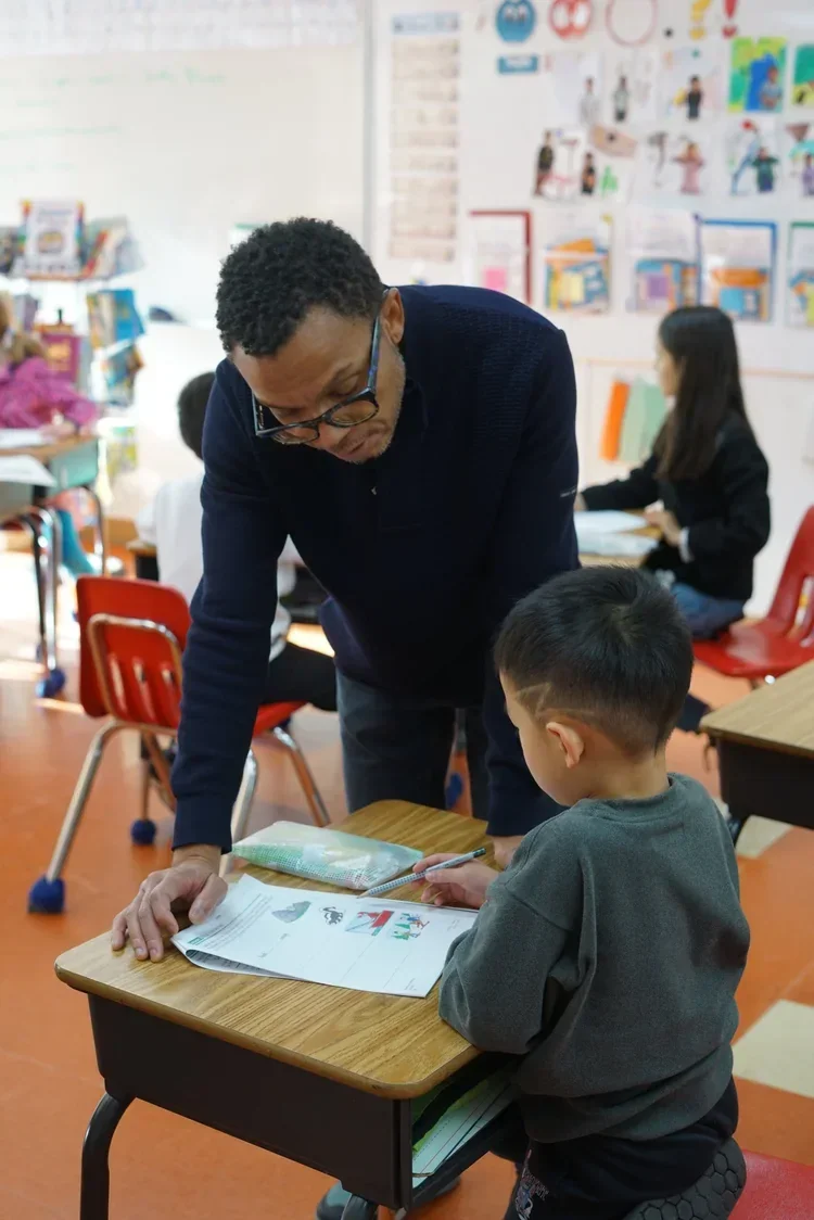 FASPS teacher helping a young student with a lesson in a bilingual classroom