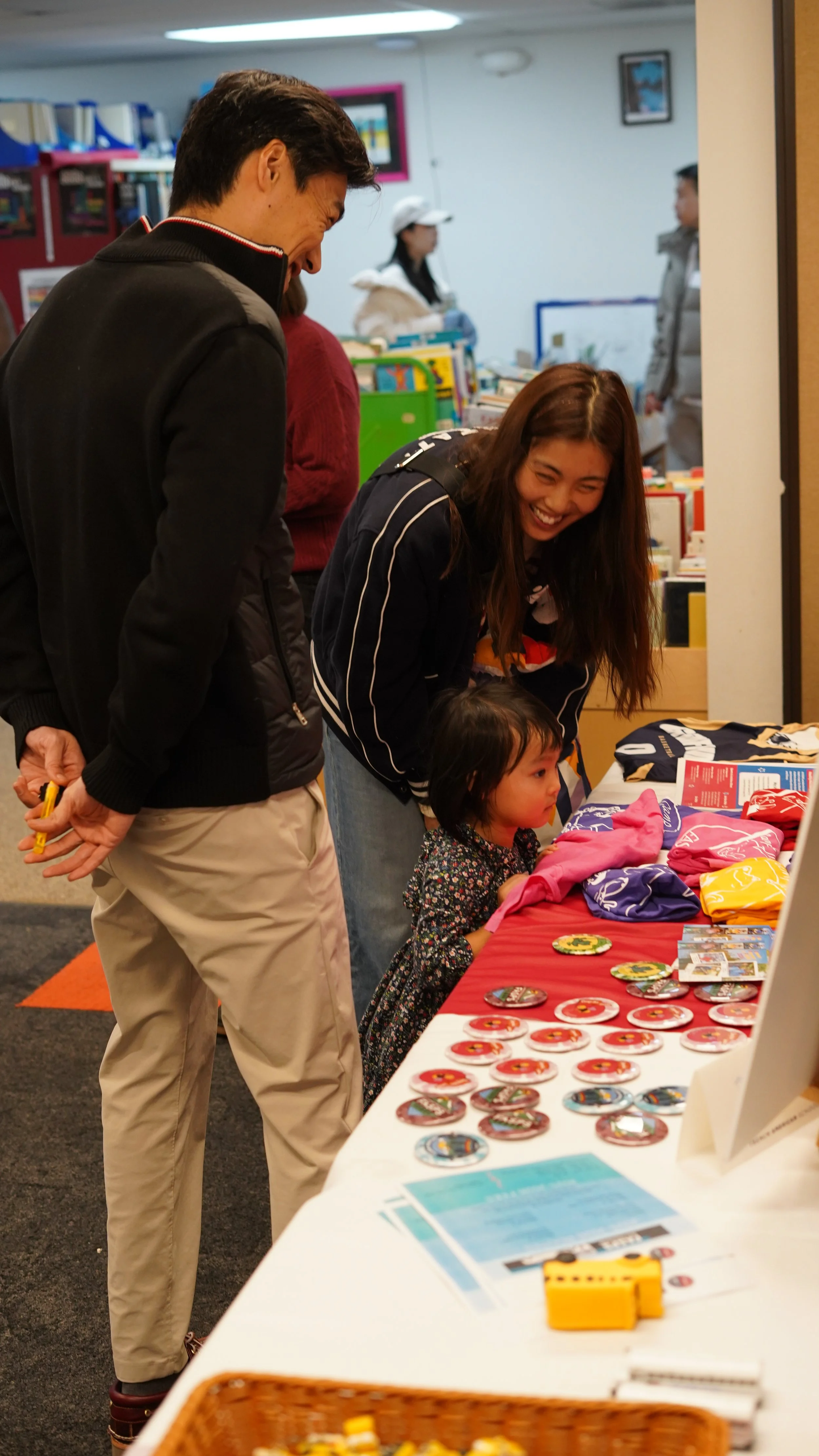 A girl at a table with colorful buttons and patches, with three adults and a young boy looking at the items.