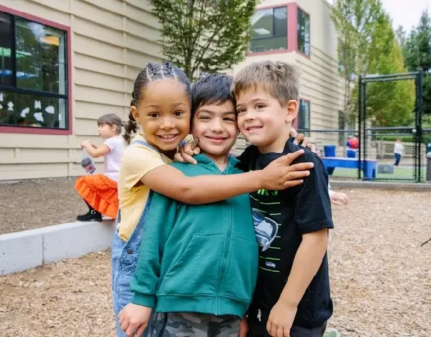 Three smiling FASPS kindergarten students hugging on the playground