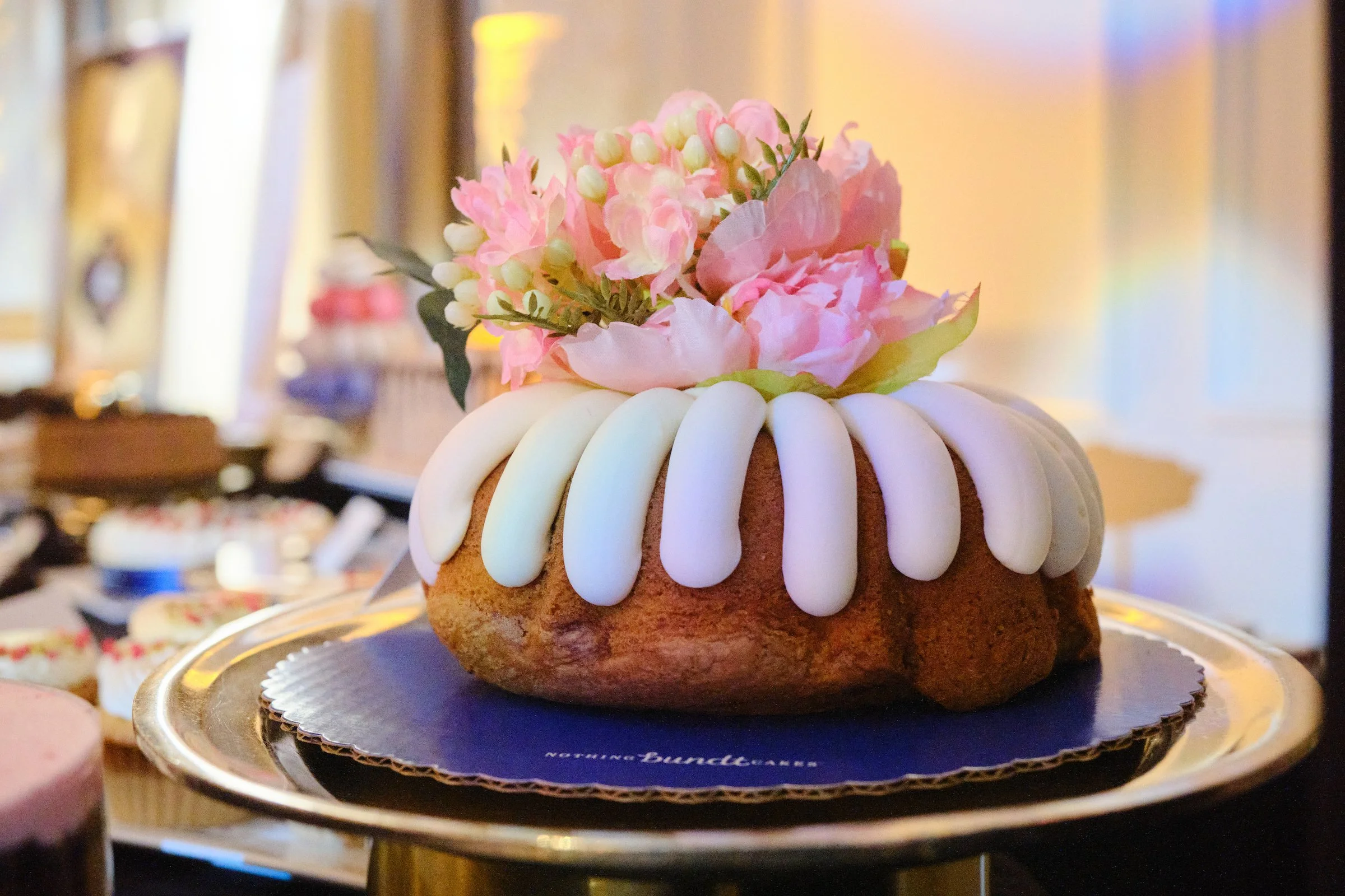 A birthday cake with white icing and pink floral decorations on top, placed on a silver cake board.