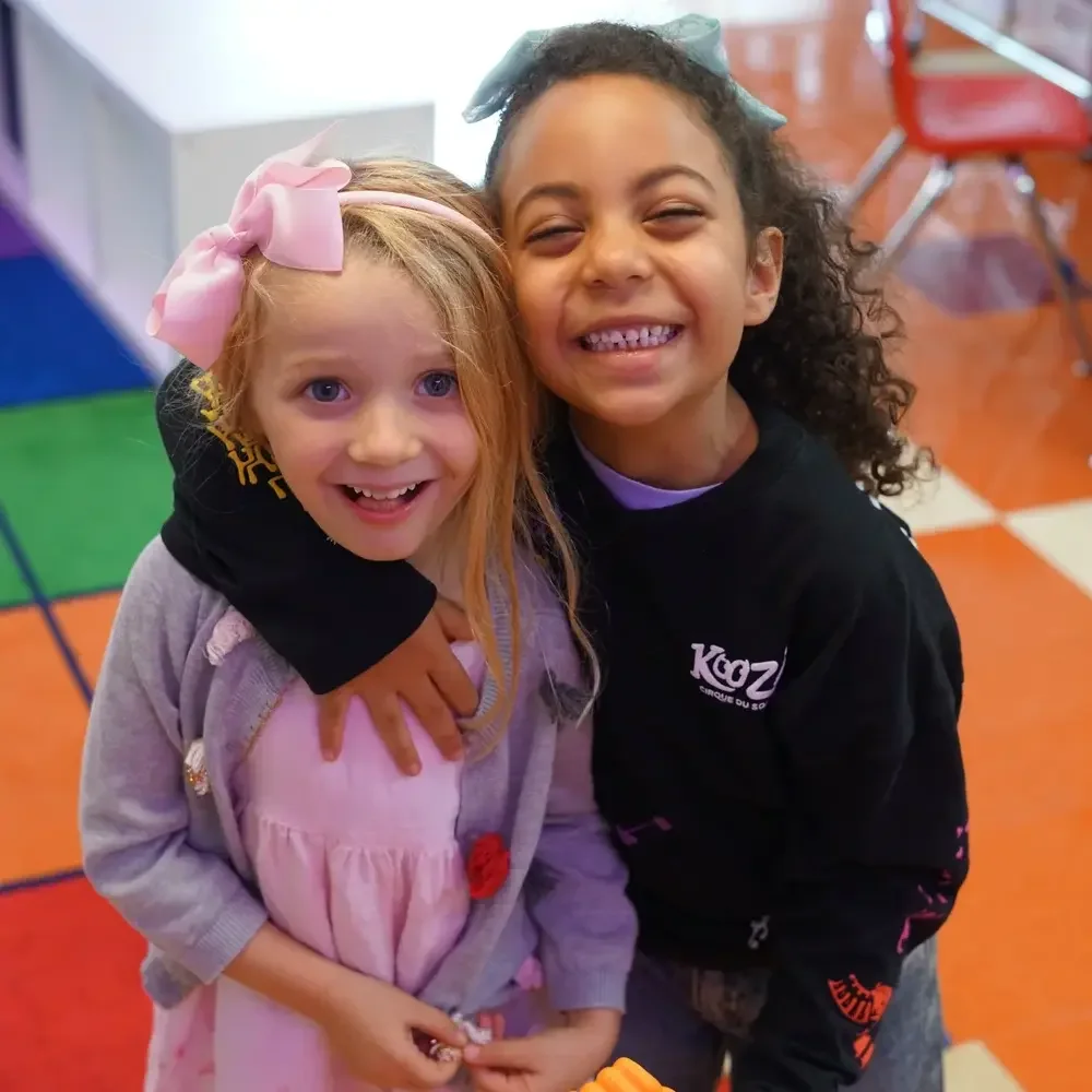 Two girls hugging in a colorful indoor play area
