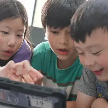 Three students smiling at a tablet in class