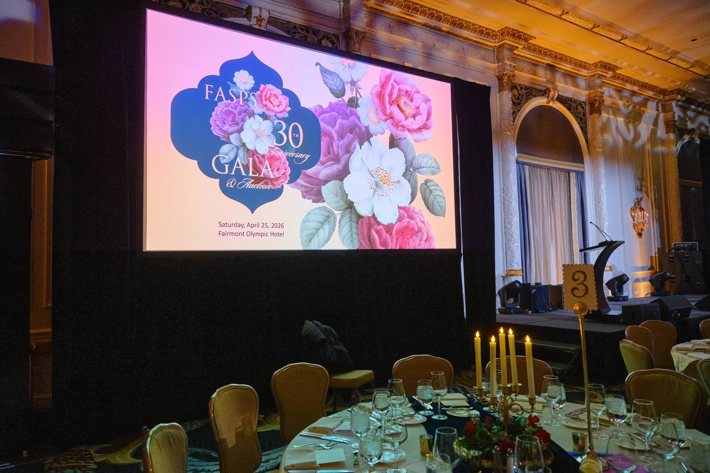 A large screen displays a floral design with text celebrating the 30th anniversary of the FASPS Gala and Auction, scheduled for Saturday, April 25, 2026, at the Fairmont Olympic Hotel. The image shows part of an ornate, elegant banquet room with deco