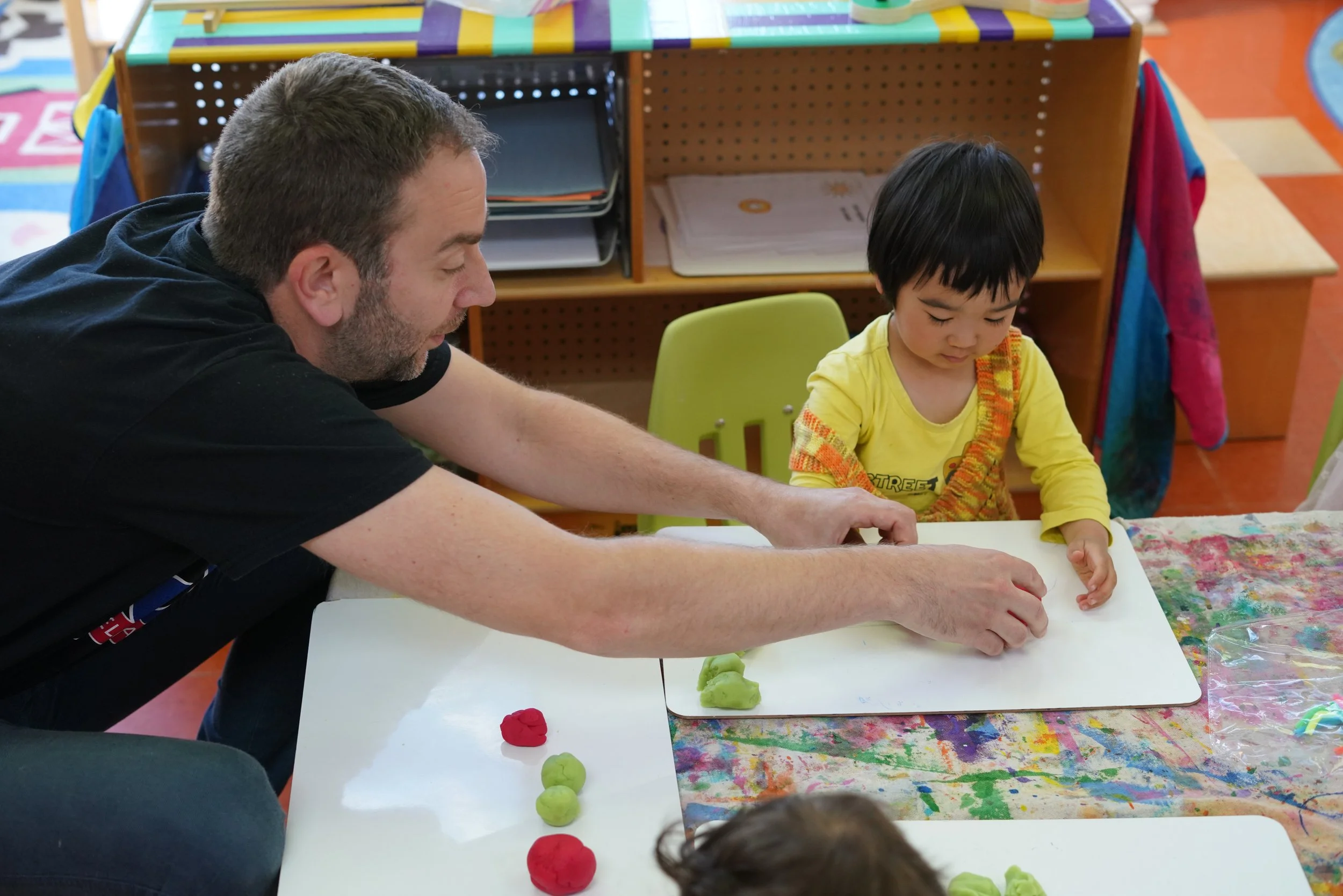Male teacher helps a young student form a shape with play dough.