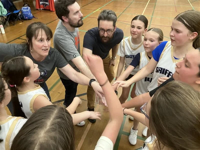 Girls' basketball team huddled with coaches in a gym, showing team spirit.