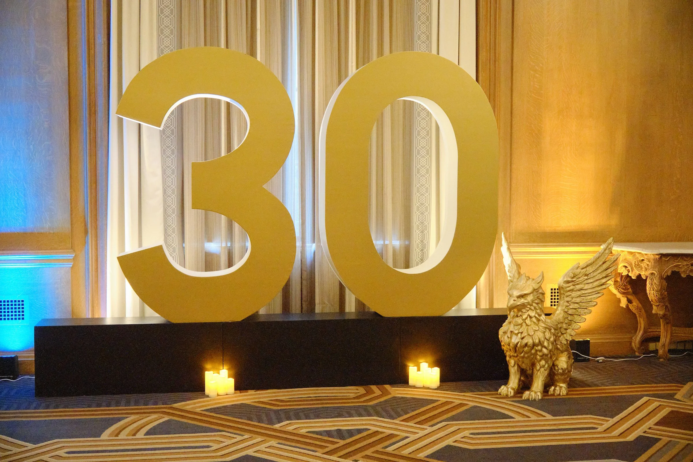 Large gold number '20' sign on a wooden wall, with a decorative golden eagle sculpture and lit candles in the foreground.