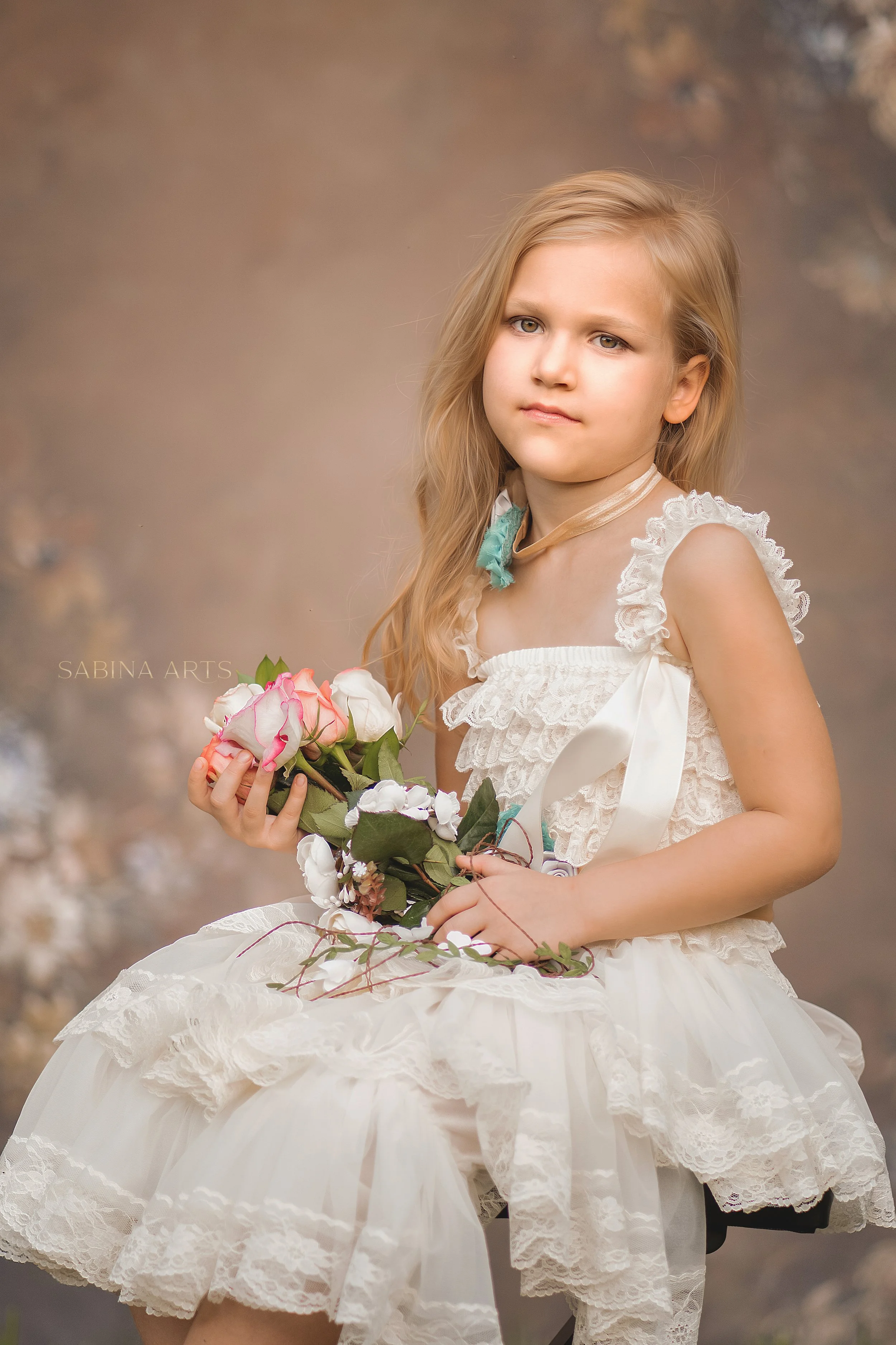 A young girl in a fancy white dress holding a bouquet of pink and white roses, posing in front of a soft blurred background.