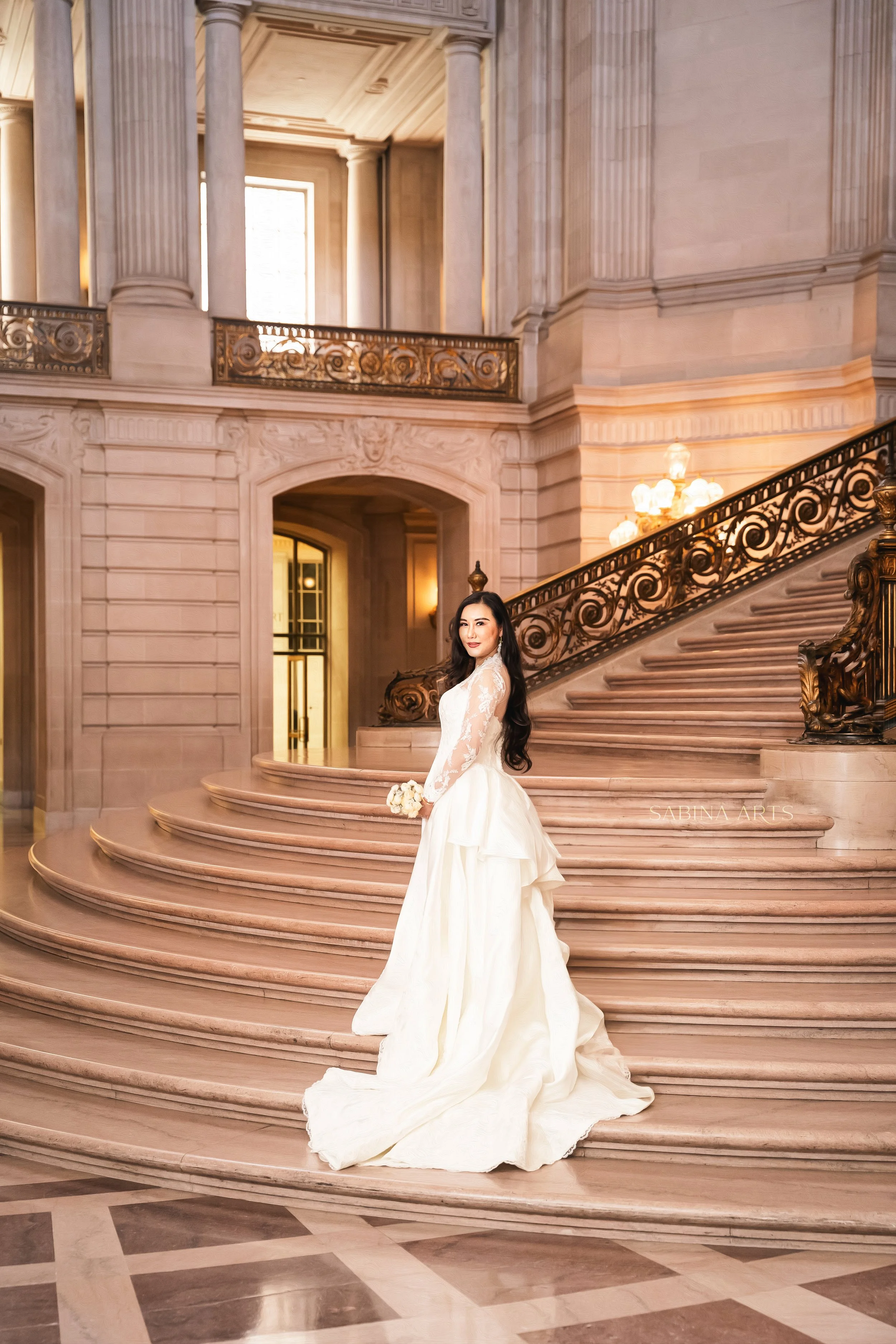 A woman in a white wedding dress stands on a grand staircase inside a luxurious building with classical architecture and ornate details.