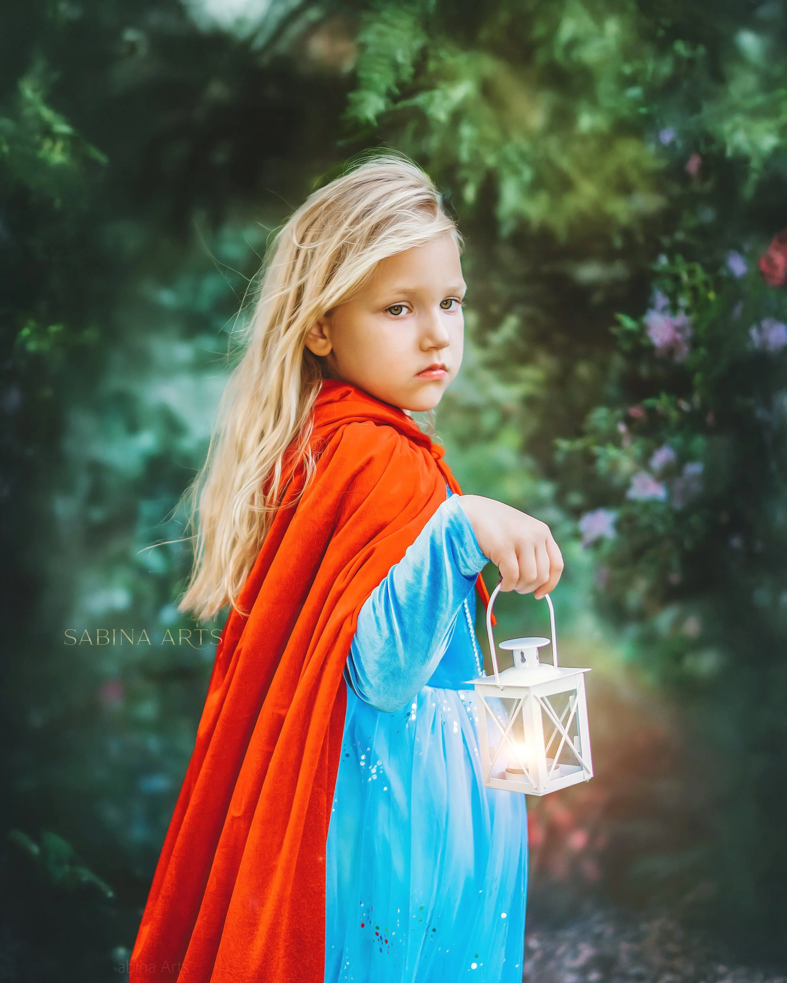 Young girl with blonde hair wearing a blue dress and red cape, holding a white lantern in a forest with greenery and flowers in the background.