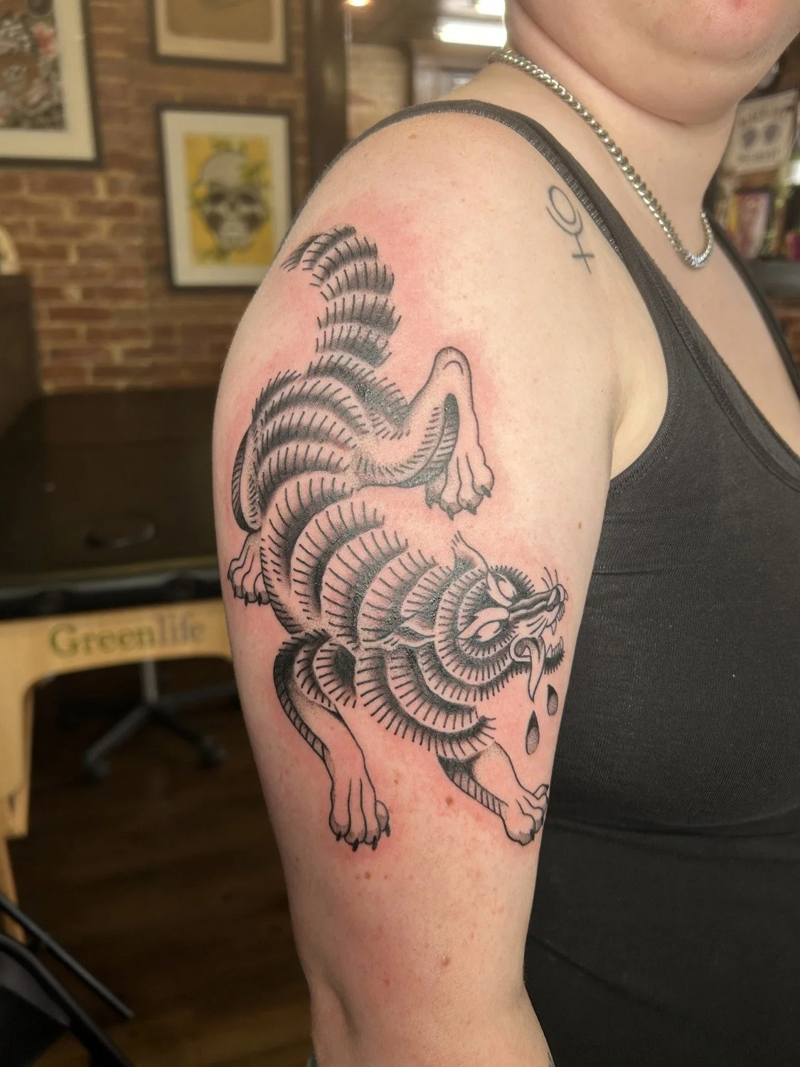 Black outline tattoo of a rat on a person's upper arm, with a striped tail, and drops of water or sweat beneath.