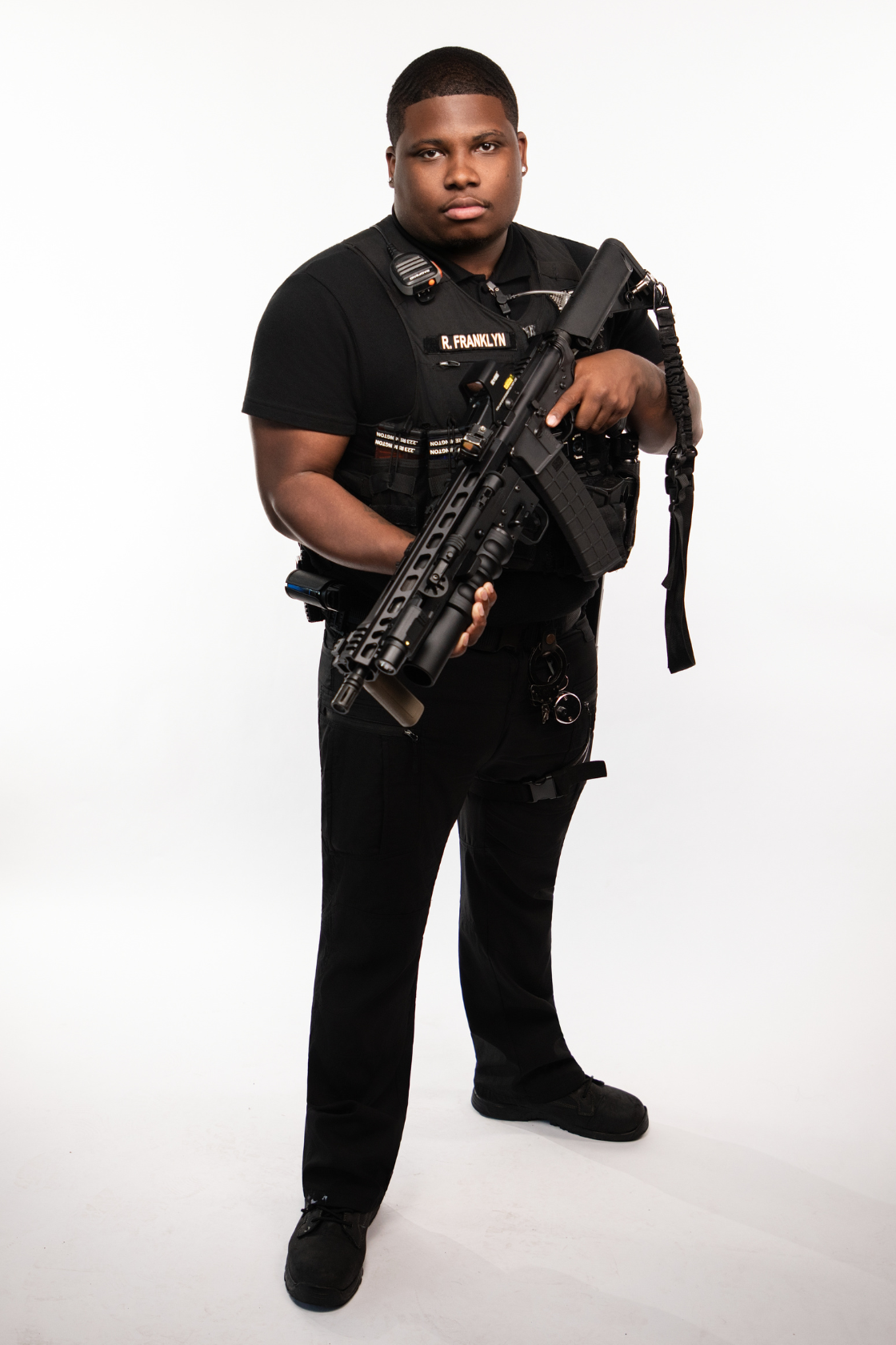 A young police officer wearing a black uniform holding a tactical shotgun.