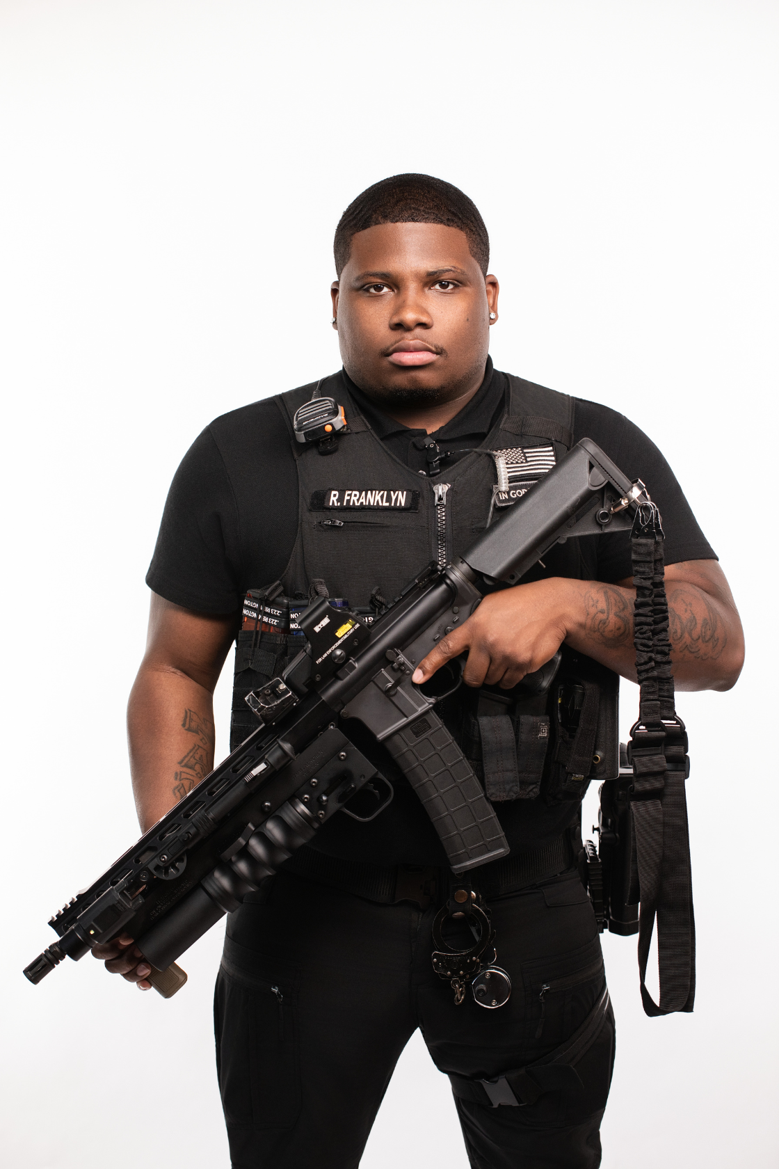 Armed police officer in tactical gear holding a rifle, against a plain white background.