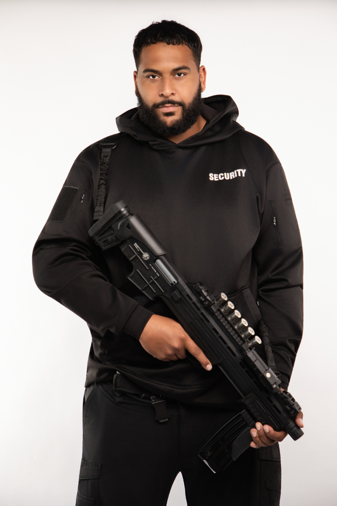 A security guard holding a large firearm, wearing a black jacket with 'SECURITY' written on it, against a plain white background.