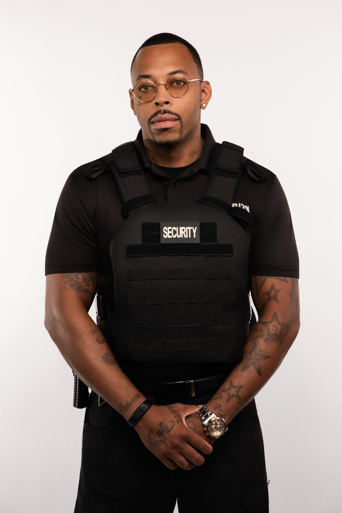 A male security guard wearing glasses and a black uniform with a tactical vest labeled 'SECURITY' stands against a white background.