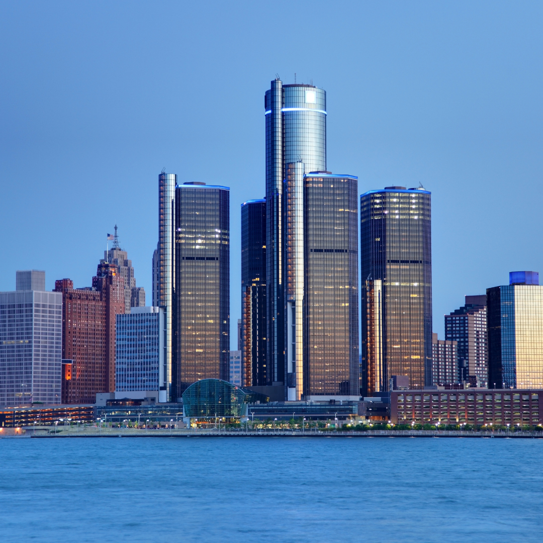 Skyline of downtown skyscrapers along a river at dusk, featuring reflections on glass buildings.
