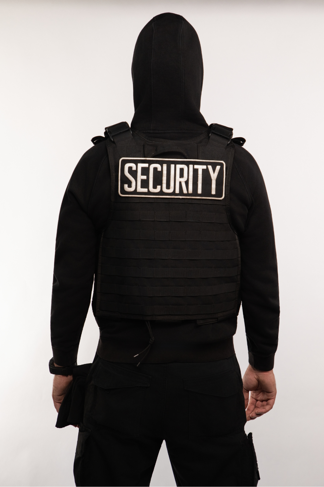 Person dressed in black security uniform with a hood and a vest labeled "SECURITY" on the back, standing against a plain white background.