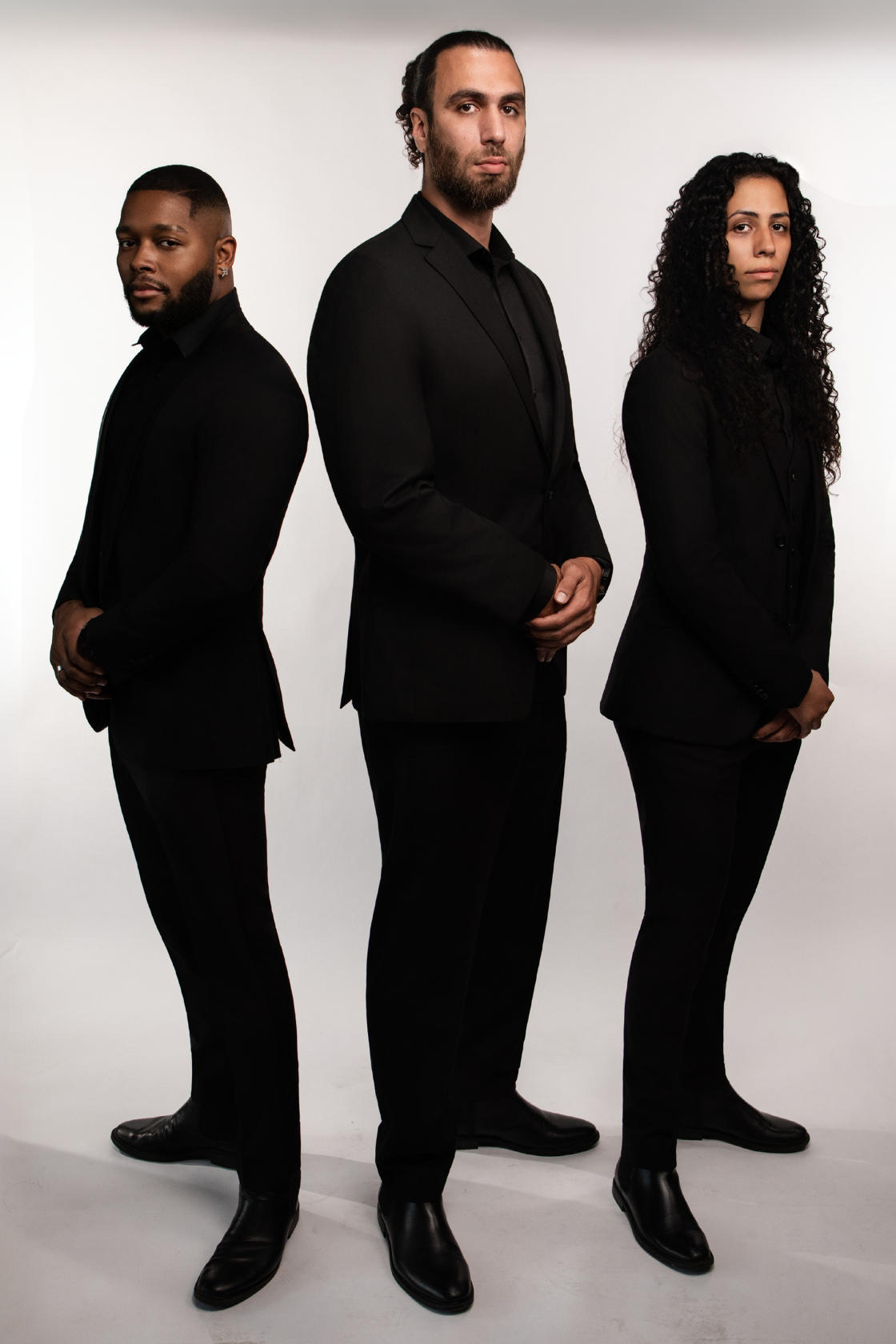 Three people in black suits standing in a row against a white background, posing for a photo.