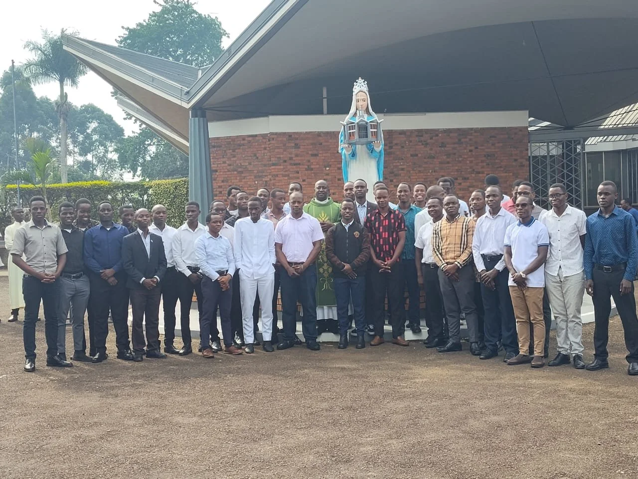 Group of men standing in front of a building with a religious statue in the background.