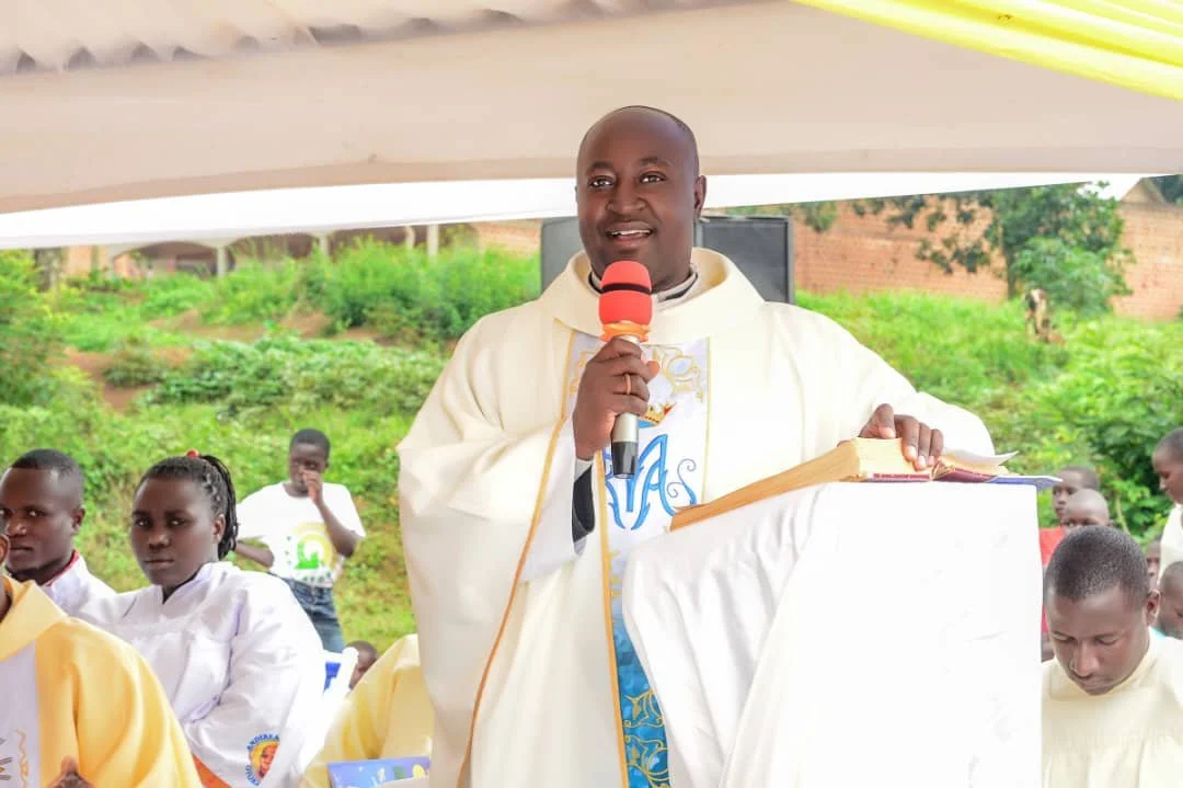A priest speaking into a microphone during an outdoor church service with children in the background