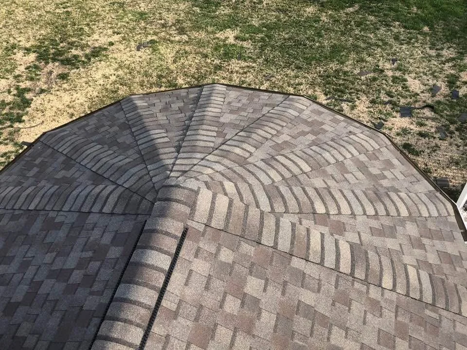 A rooftop with gray shingles and a unique pattern, viewed from above, with a grassy yard in the background.