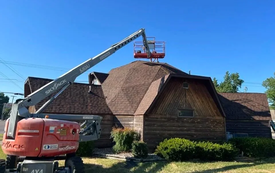 A lift working on the roof of a wooden house during daytime, with a clear blue sky in the background.