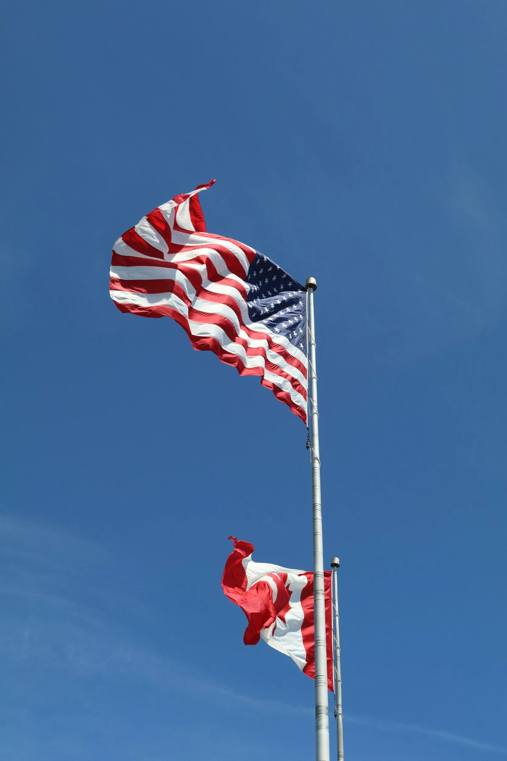 American flag flying high on a flagpole against a clear blue sky with some wispy clouds.