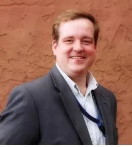 Gentleman smiling wearing a grey suit with a white shirt.