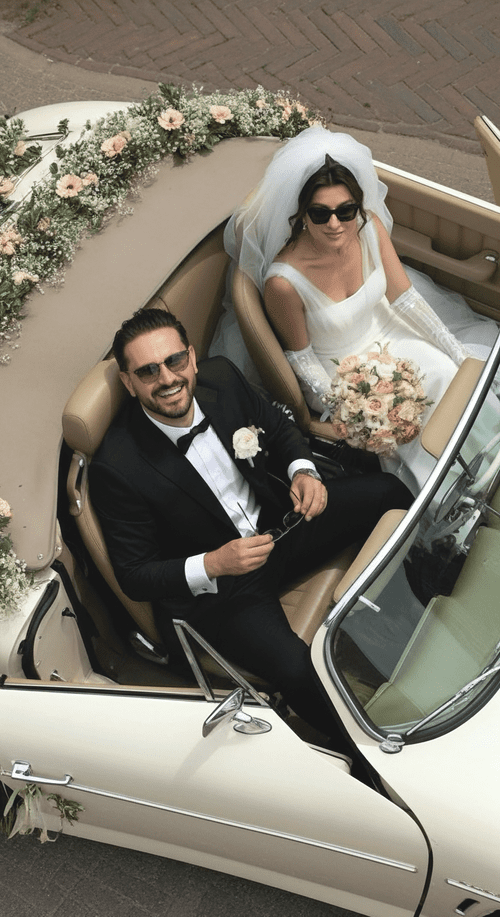 Bride and groom in a vintage convertible car, celebrating a wedding, with the bride holding a bouquet of flowers and wearing sunglasses and a white wedding dress, groom in a tuxedo with a boutonniere, decorated with flowers on the car.